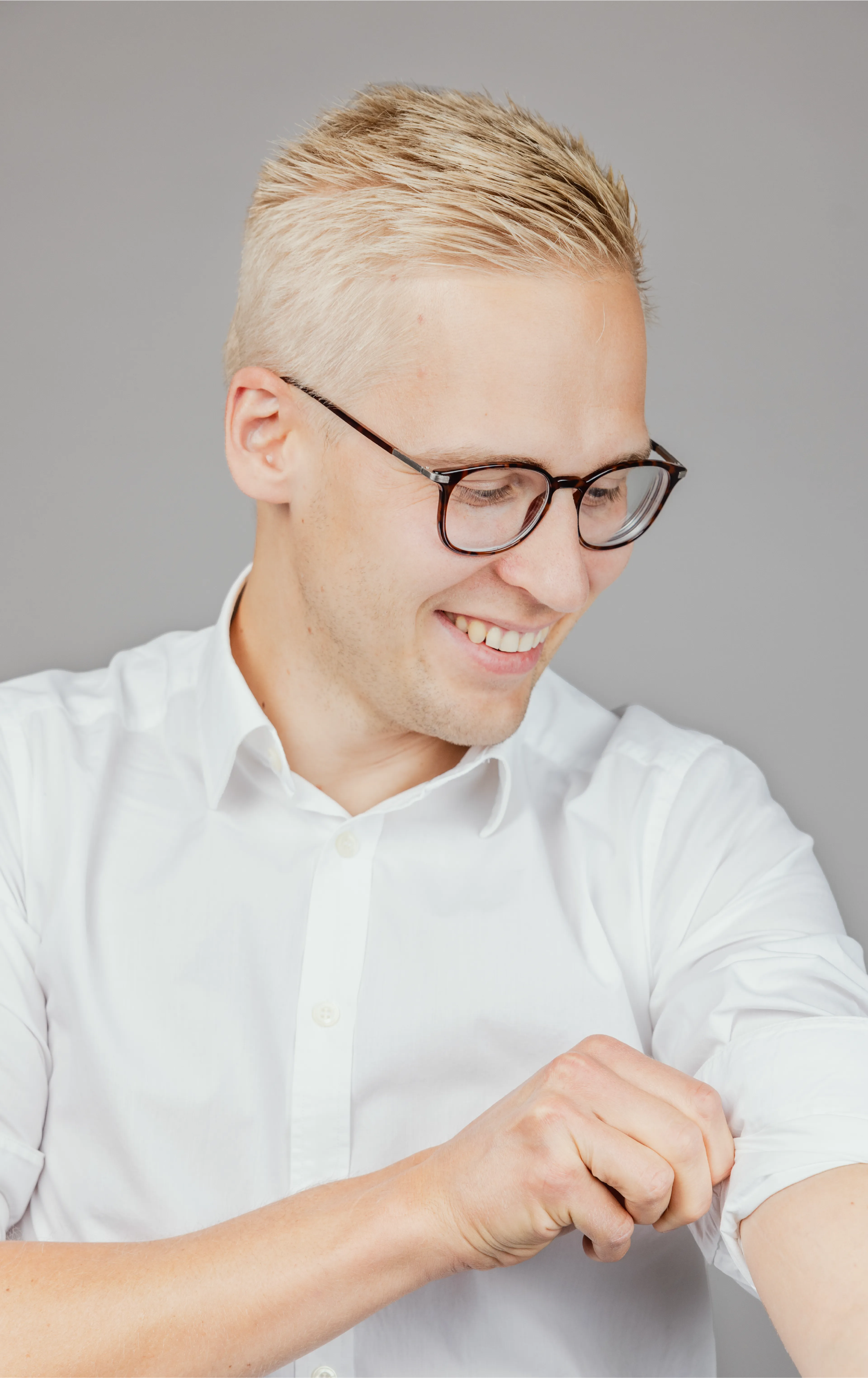 A man with glasses, rolling up the sleeve of his shirt
