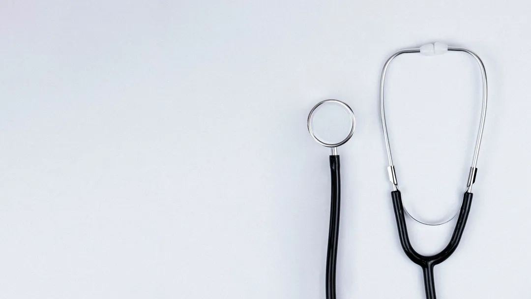 Blue stethoscope and blue pens resting on the pocket of a white medical lab coat, symbolizing healthcare and the medical profession