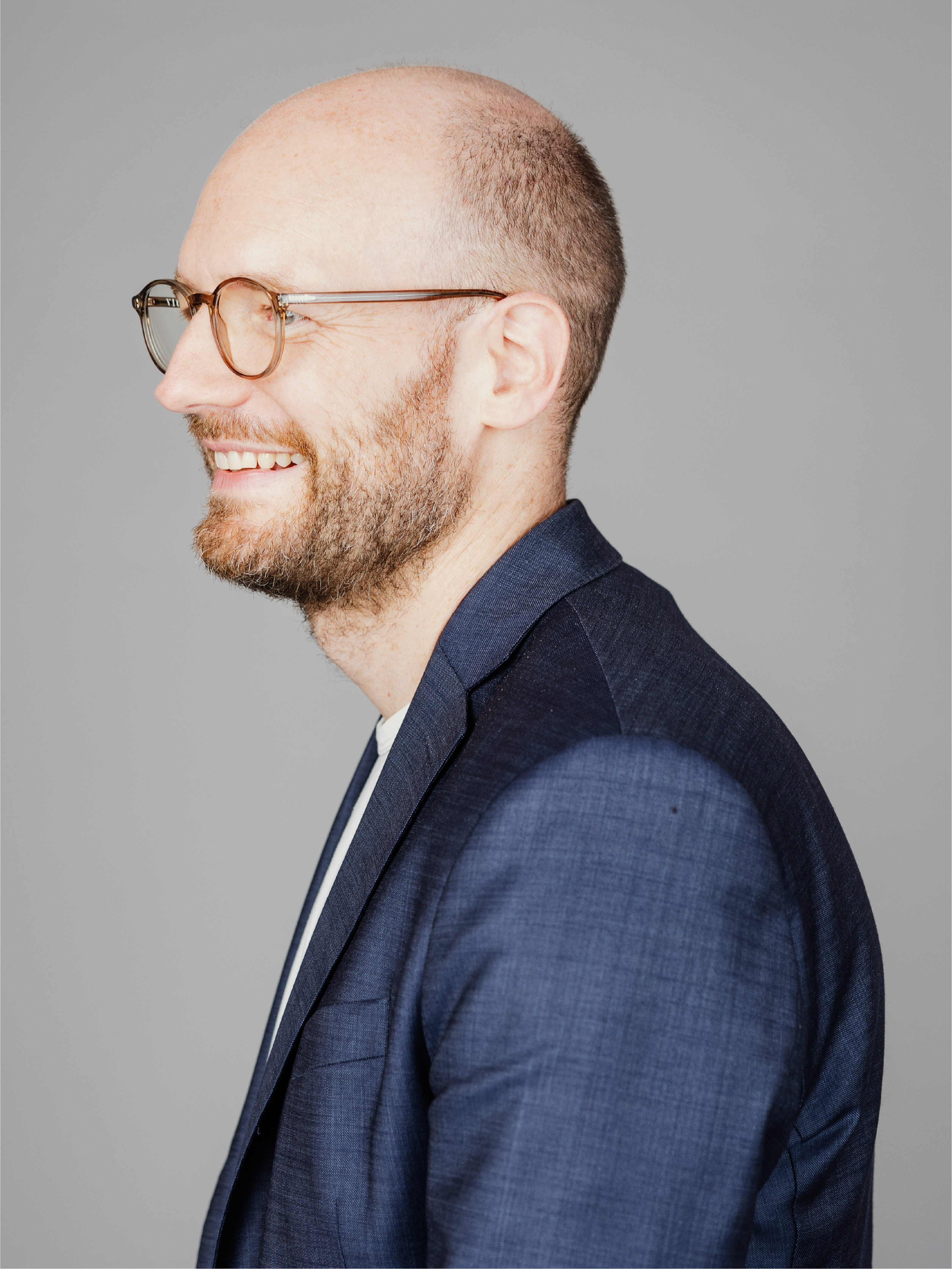 A man with glasses smiling and facing the left