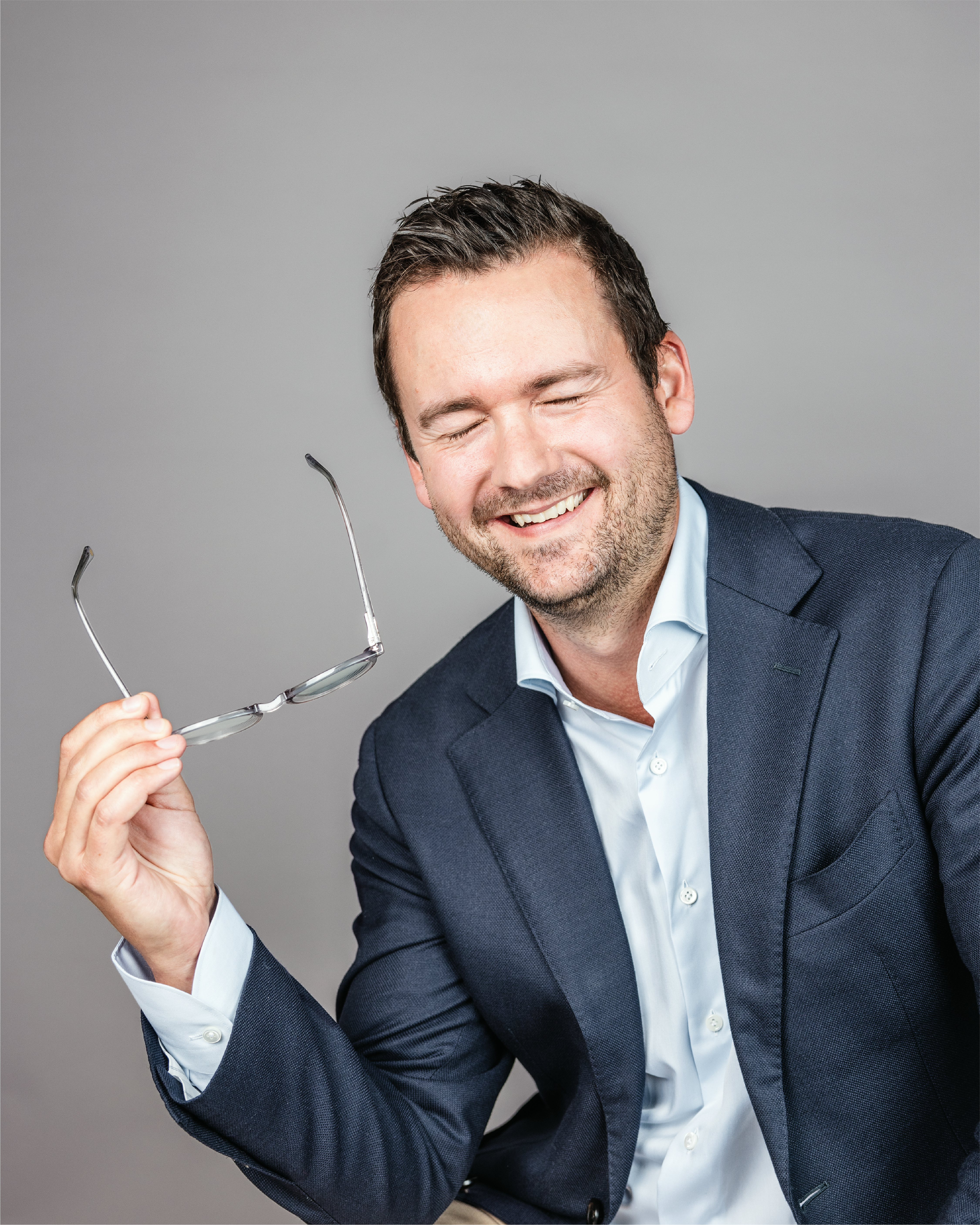 Guy with closed eyes, smiling and holding his glasses