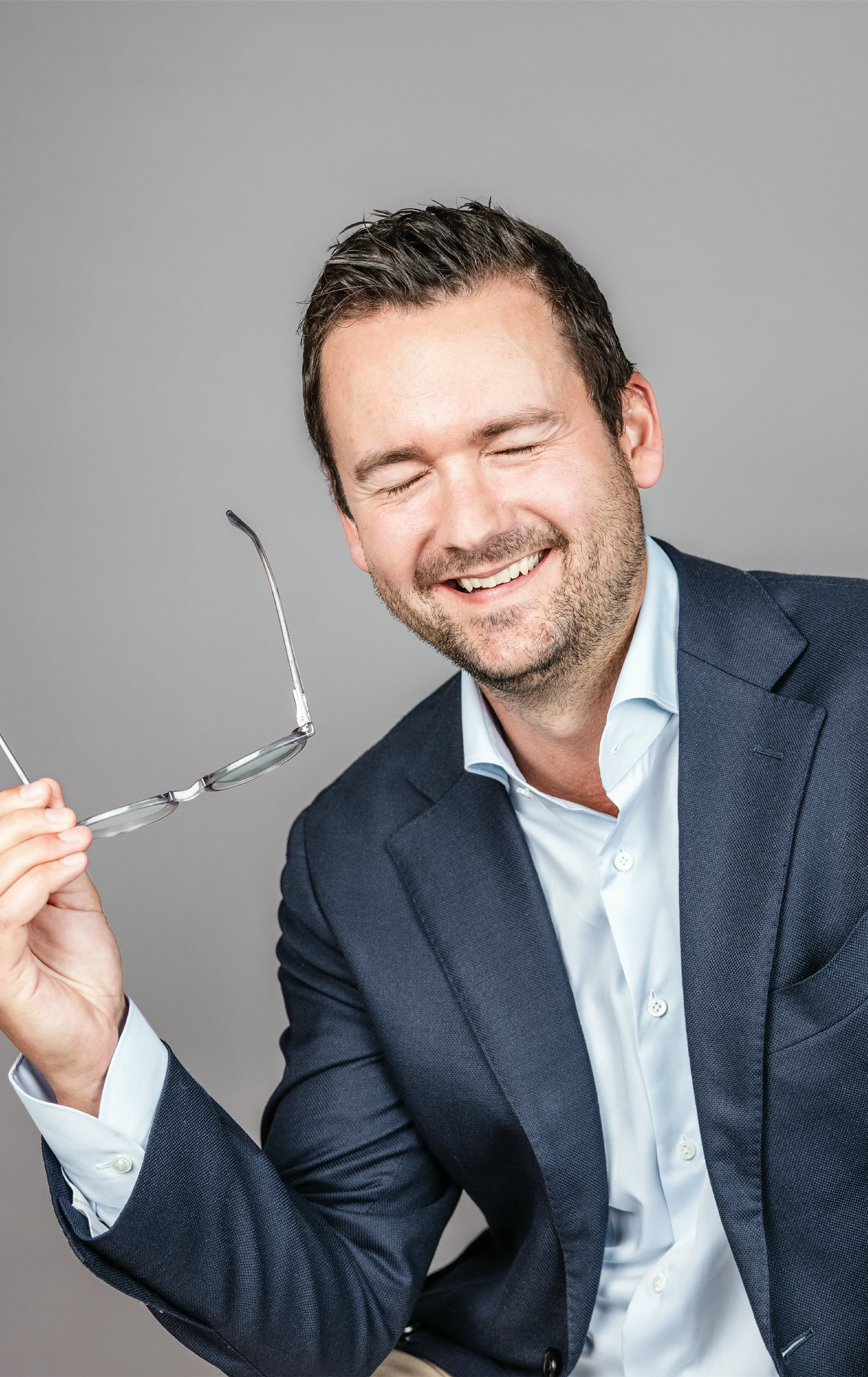 Guy with closed eyes, smiling and holding his glasses
