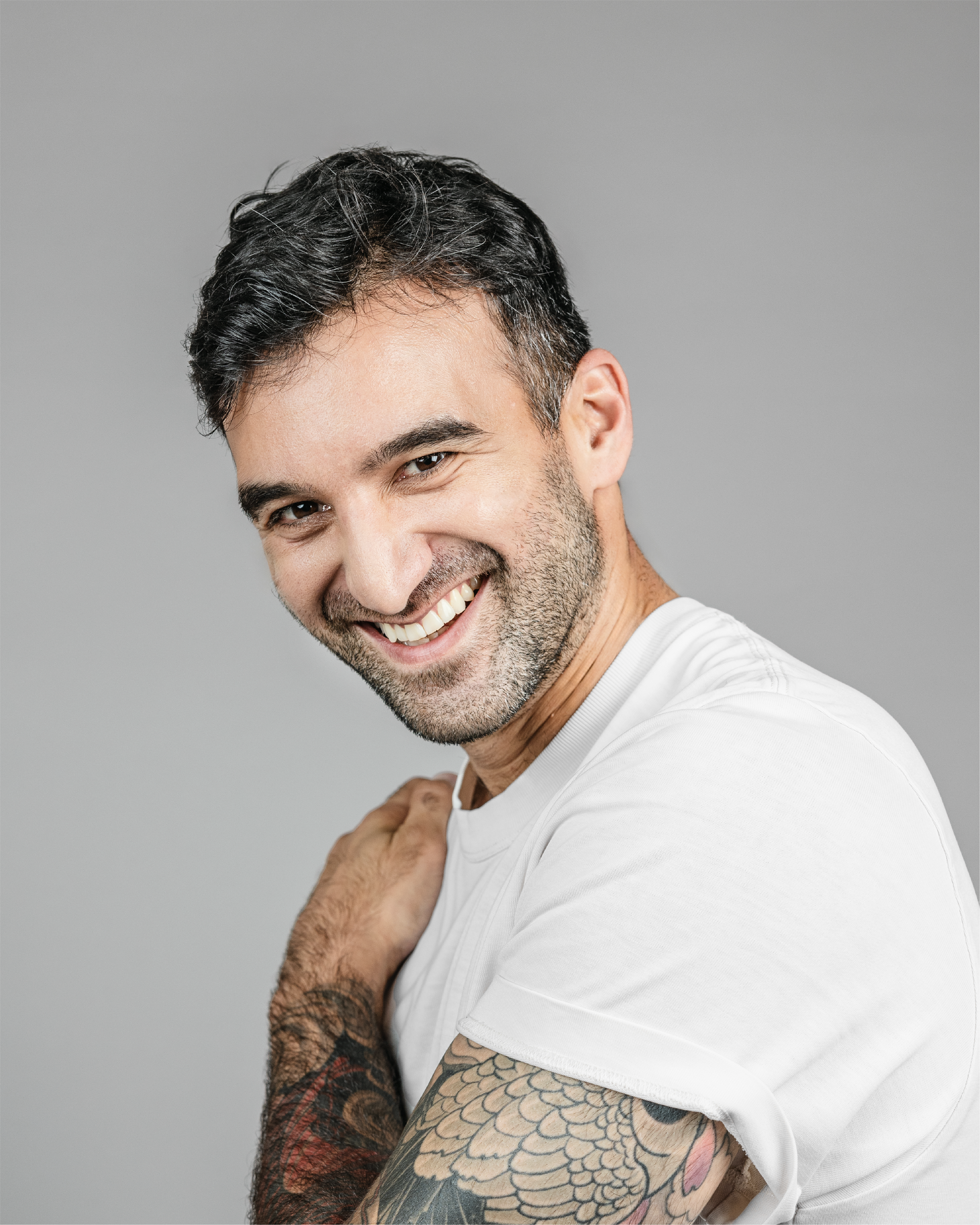 Guy with tattoos, laughing, holding a hand on his shoulder