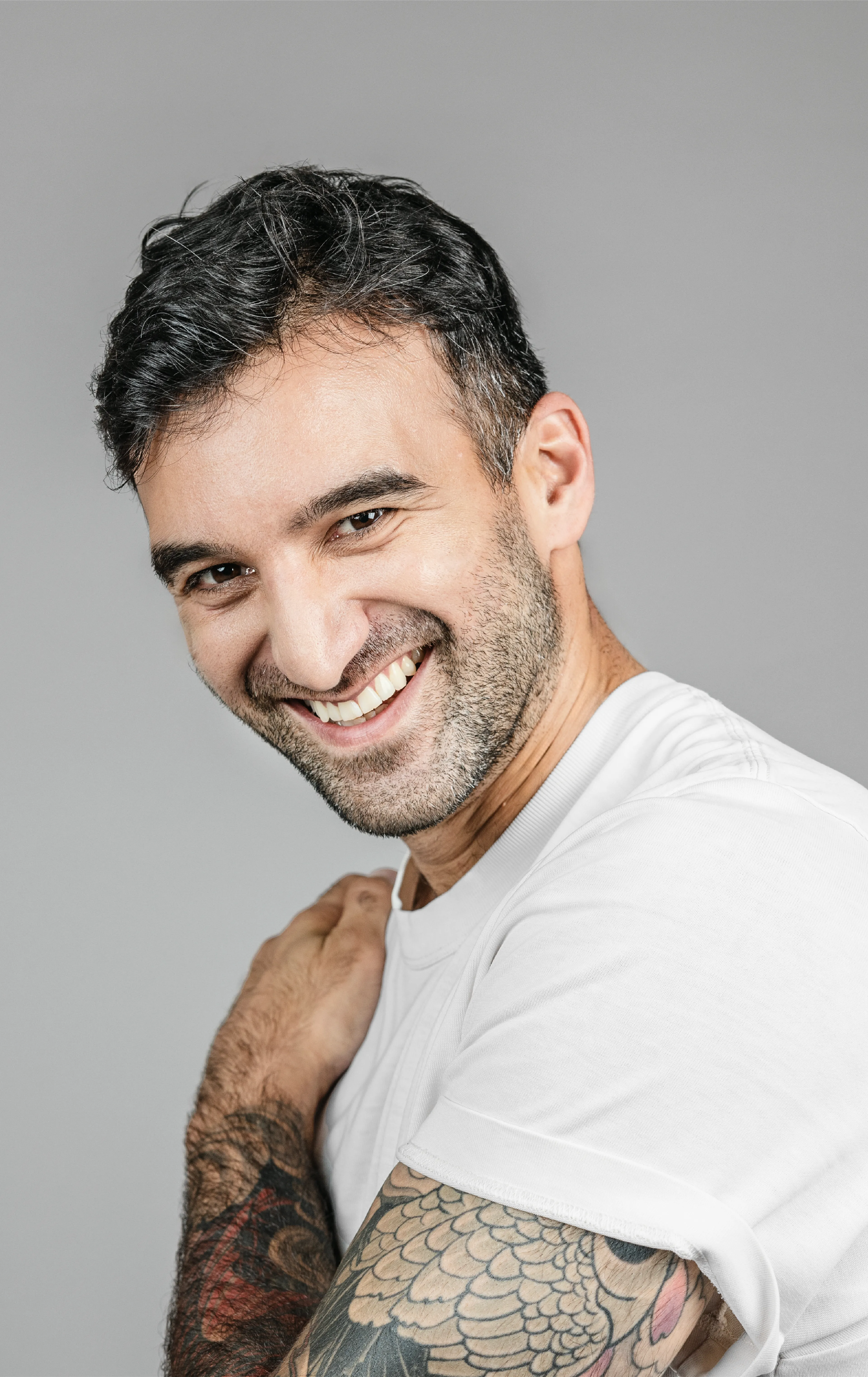 Guy with tattoos, laughing, holding a hand on his shoulder