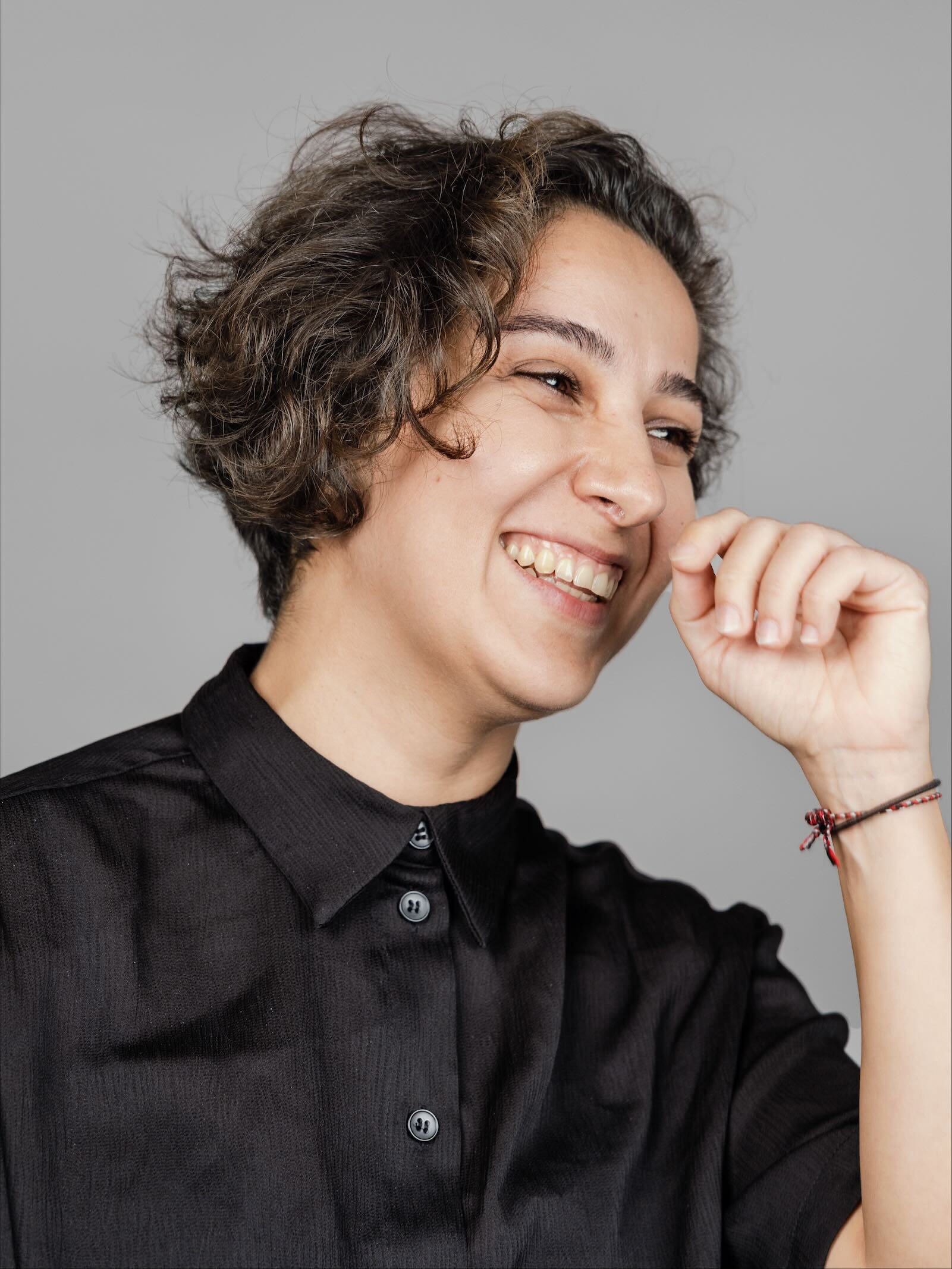 Woman facing left while smiling and holding hand towards face