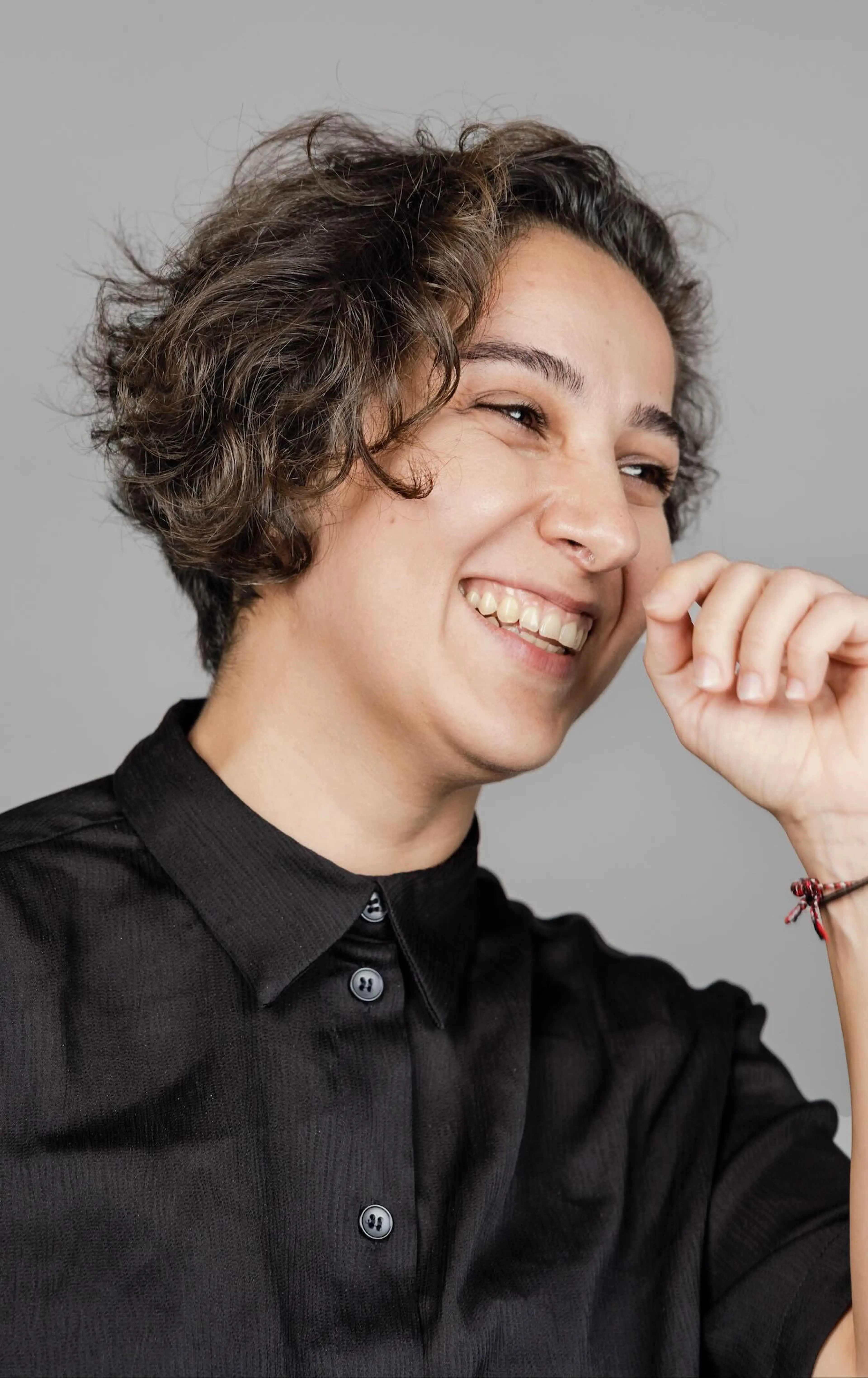 Woman facing left while smiling and holding hand towards face