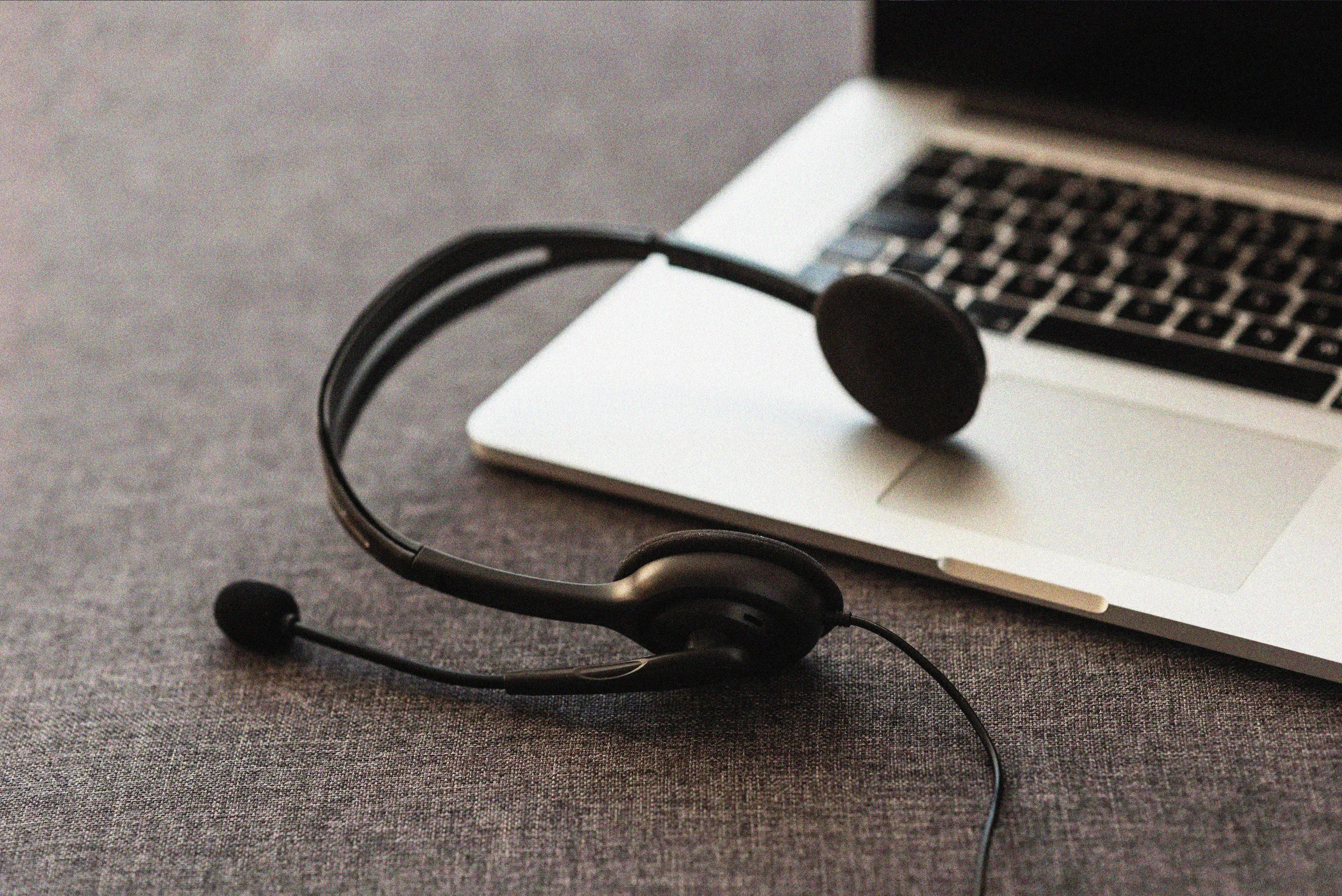  Black headset with a microphone resting on the keyboard of a silver laptop, placed on a dark surface, representing online communication or remote work
