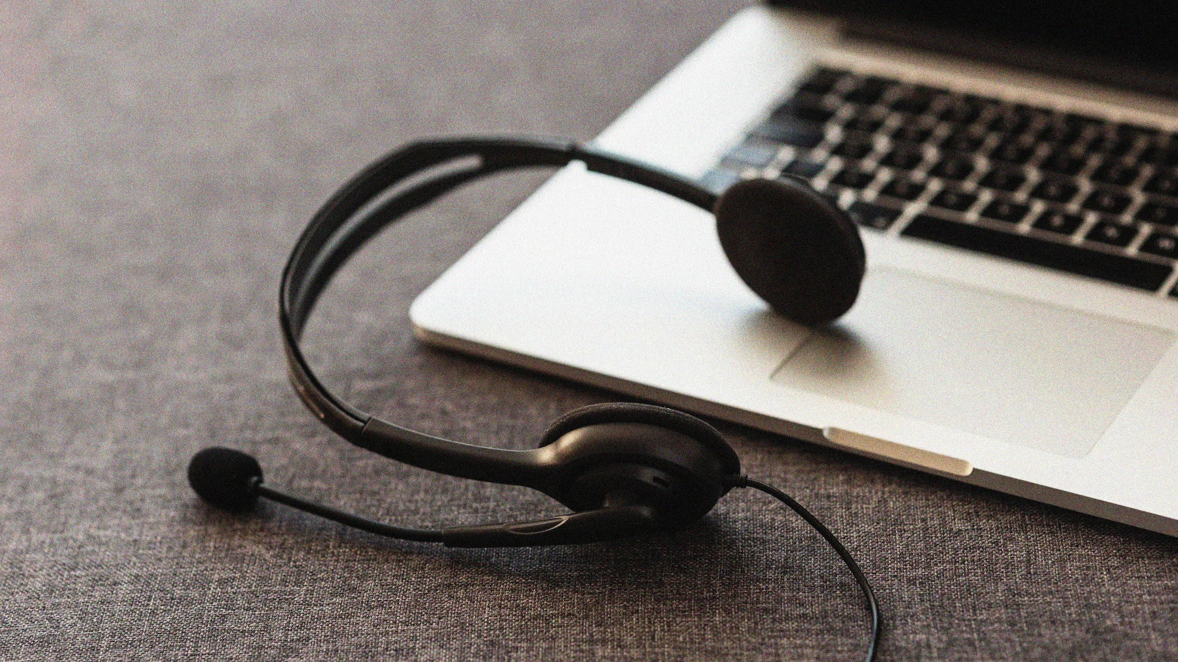  A black headset with a microphone resting on a gray surface next to an open laptop. The image suggests remote work, online communication, or customer service support.