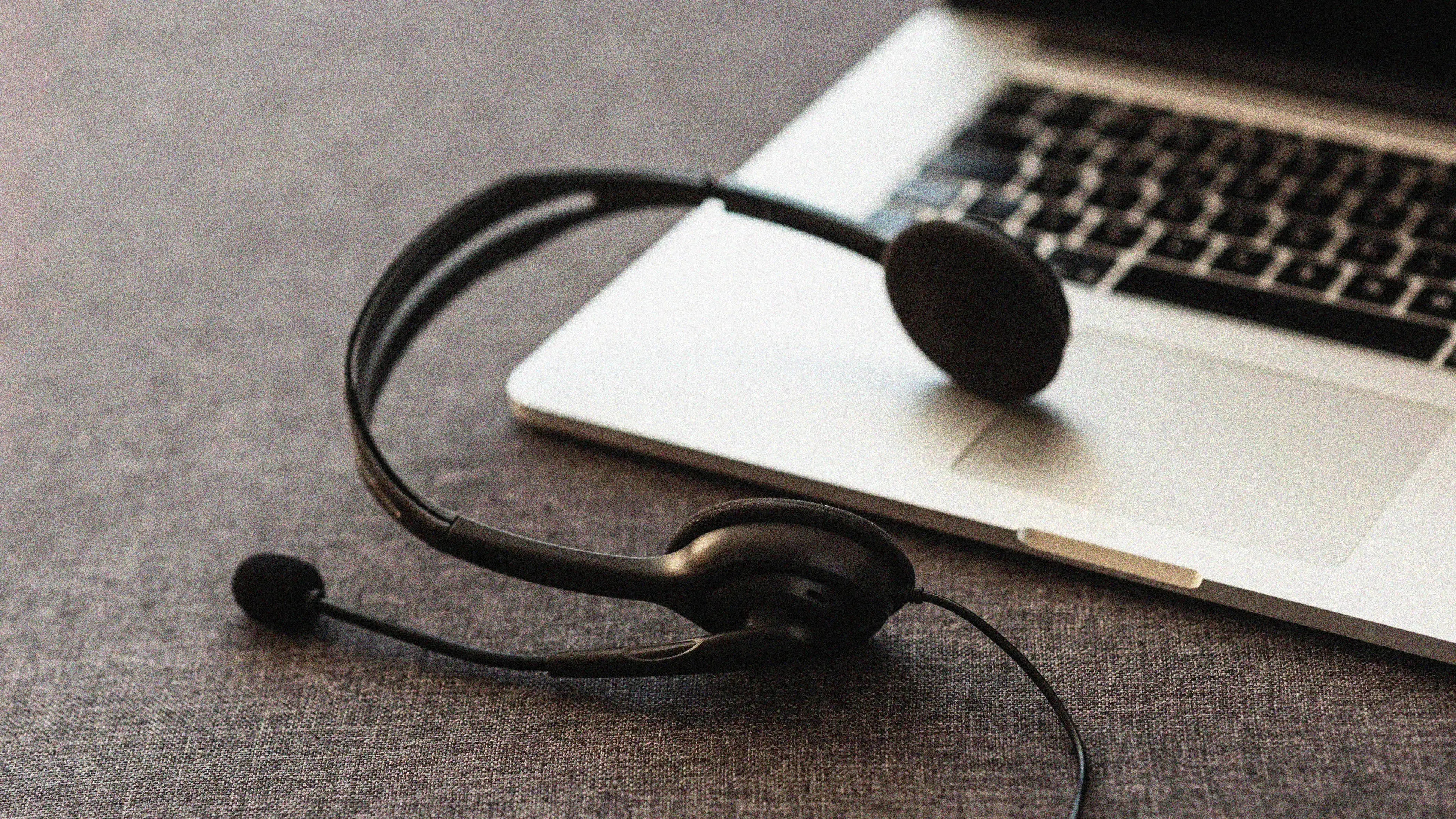  A black headset with a microphone resting on a gray surface next to an open laptop. The image suggests remote work, online communication, or customer service support.