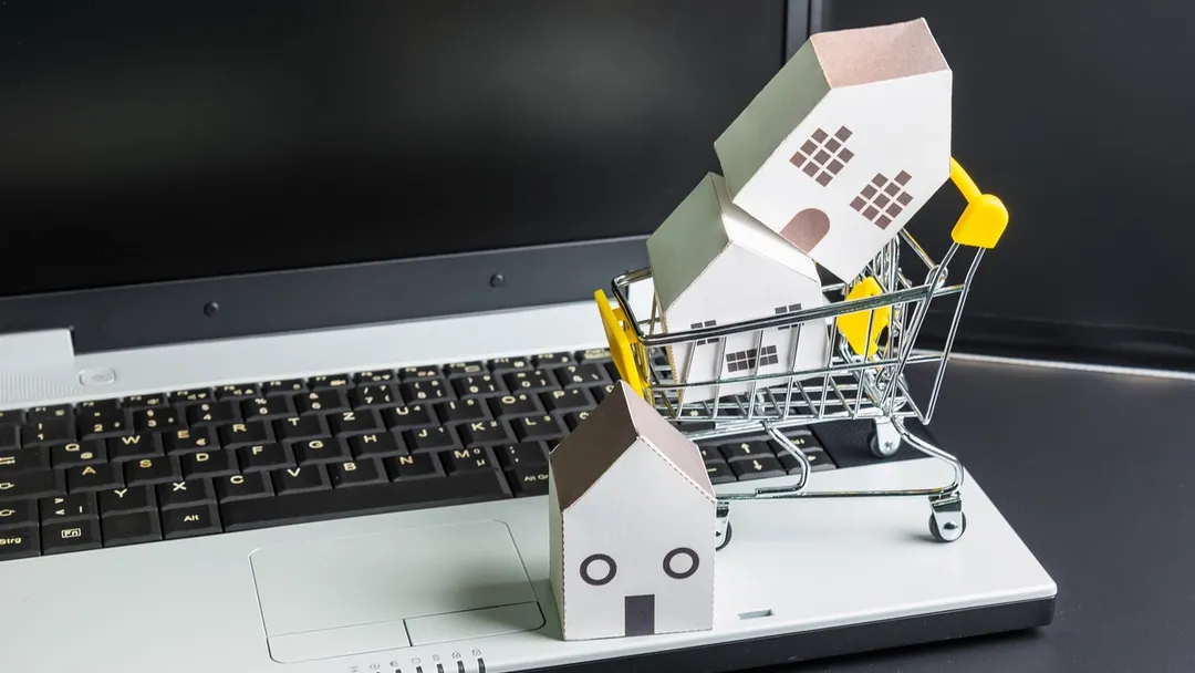 Miniature shopping cart filled with small cardboard boxes placed on top of a laptop keyboard, representing online shopping and e-commerce