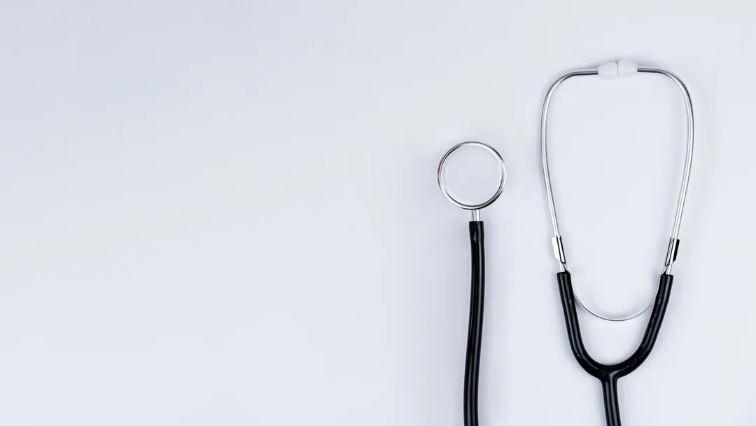 Blue stethoscope and blue pens resting on the pocket of a white medical lab coat, symbolizing healthcare and the medical profession