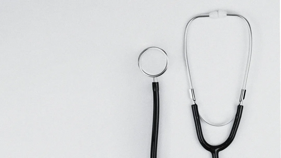 Blue stethoscope and blue pens resting on the pocket of a white medical lab coat, symbolizing healthcare and the medical profession