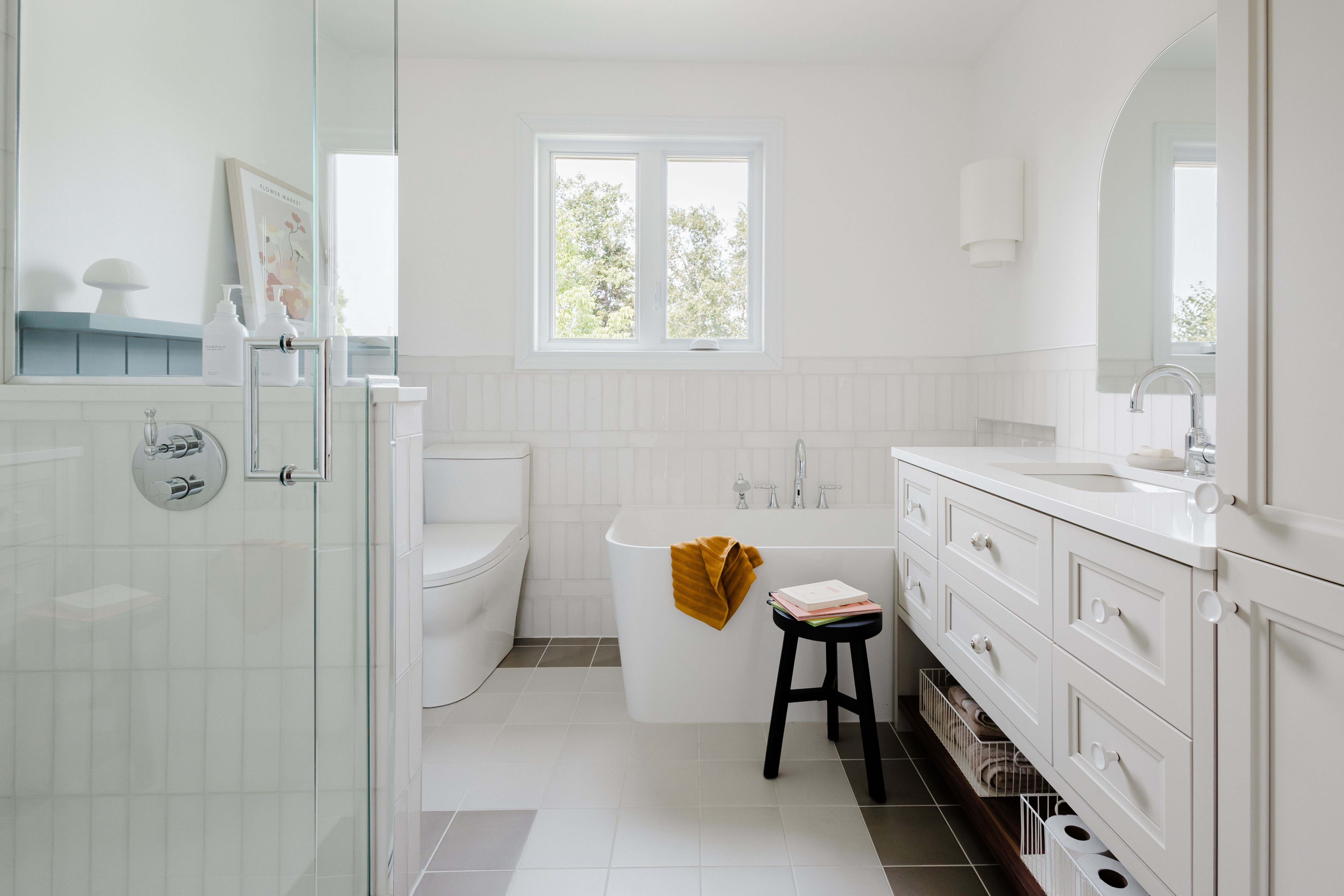 Salle de bain lumineuse, bain en coin, détail de céramique, vanité sur mesure, tuile blanche, lambris bleu, douche en verre, mirroir en arche