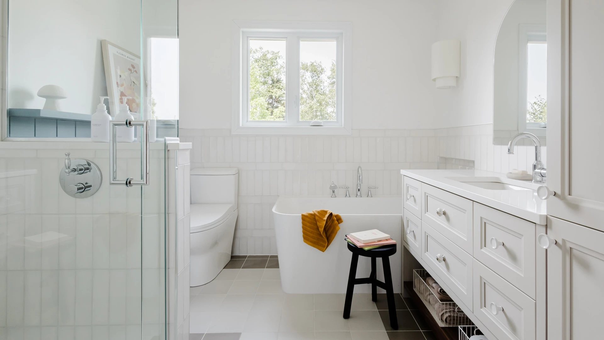 Salle de bain lumineuse, bain en coin, détail de céramique, vanité sur mesure, tuile blanche, lambris bleu, douche en verre, mirroir en arche