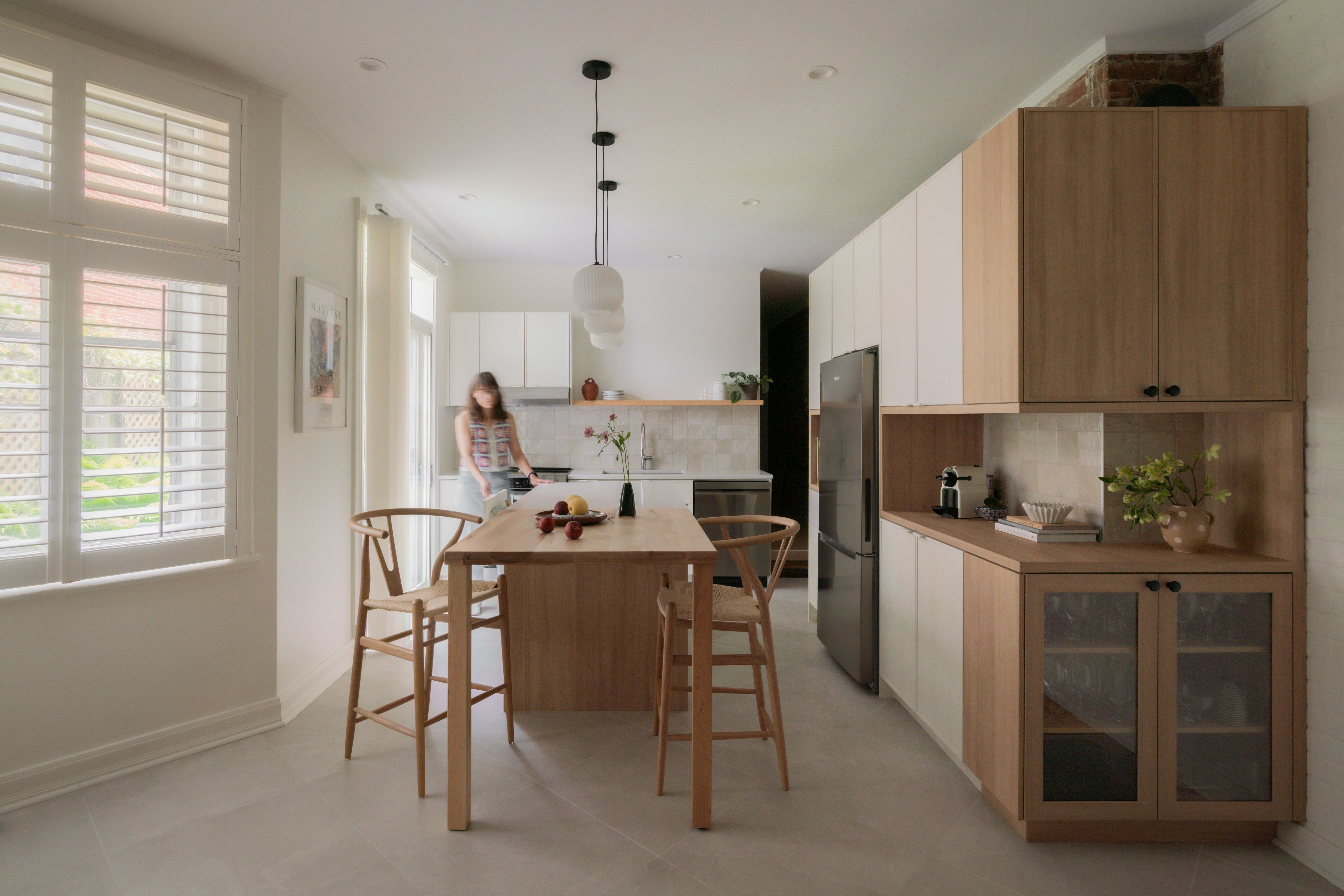 cuisine crème, îlot de bois, comptoir de quartz, tabourets de bois, armoires blanches, armoires bois, dosseret de tuiles carrées, tuiles 24x24 au sol, mur de brique