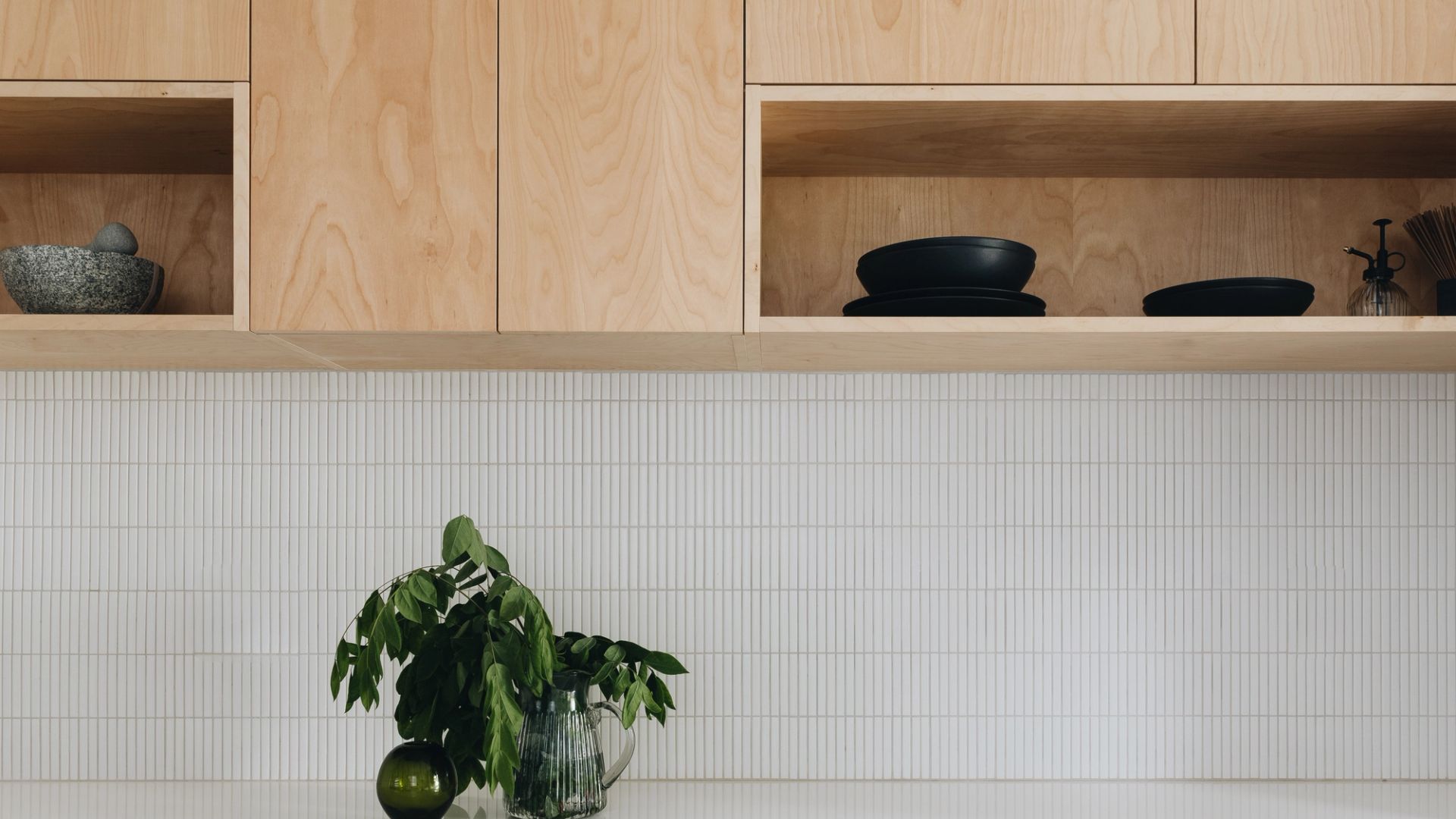 Cuisine moderne, dosseret de tuiles "stick" et armoire de bois, décoration de branche vertes dans un vase en verre