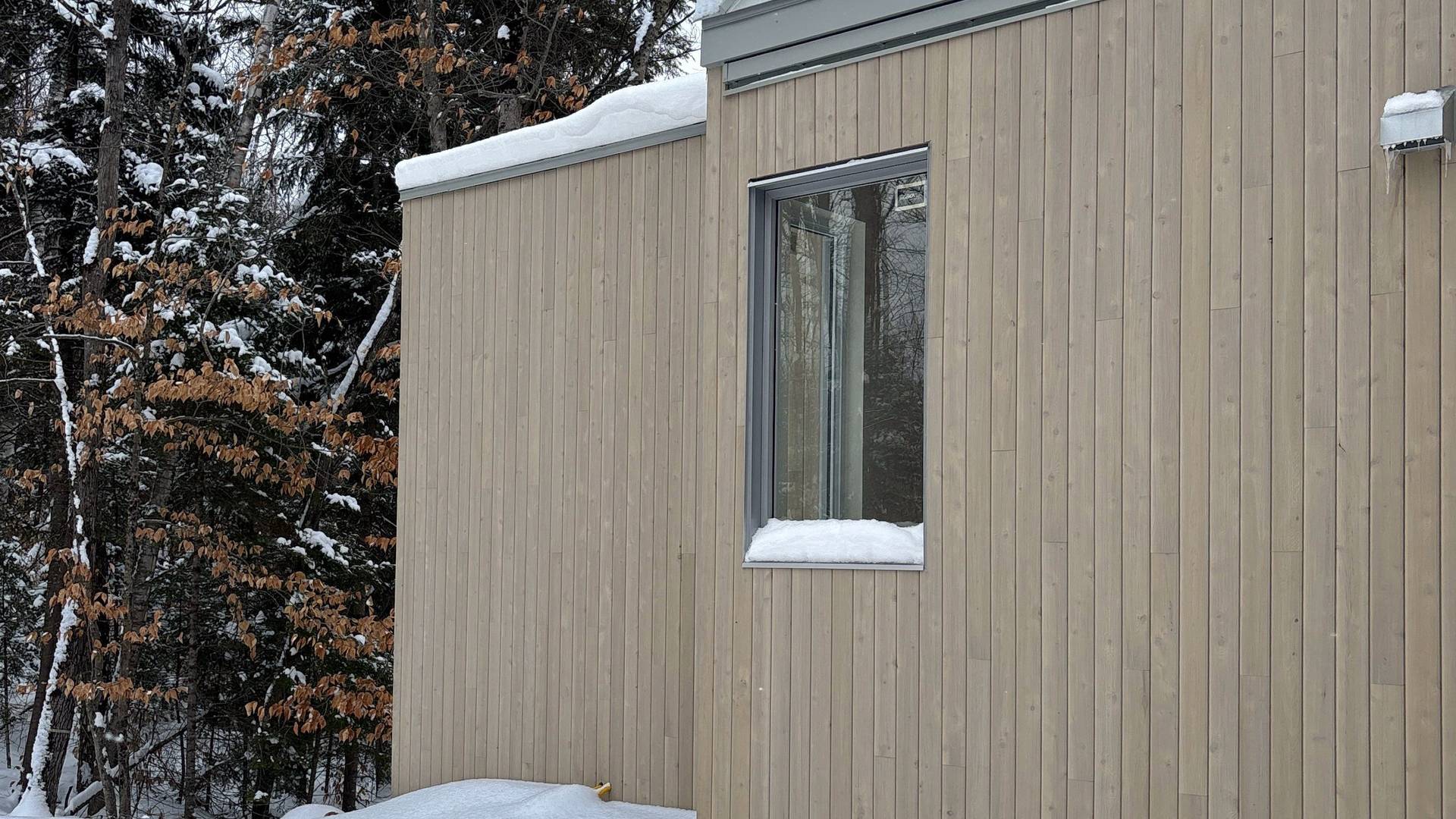 maison en construction, revêtment de bois pâle toiture d'acier grise environnement en nature et neige