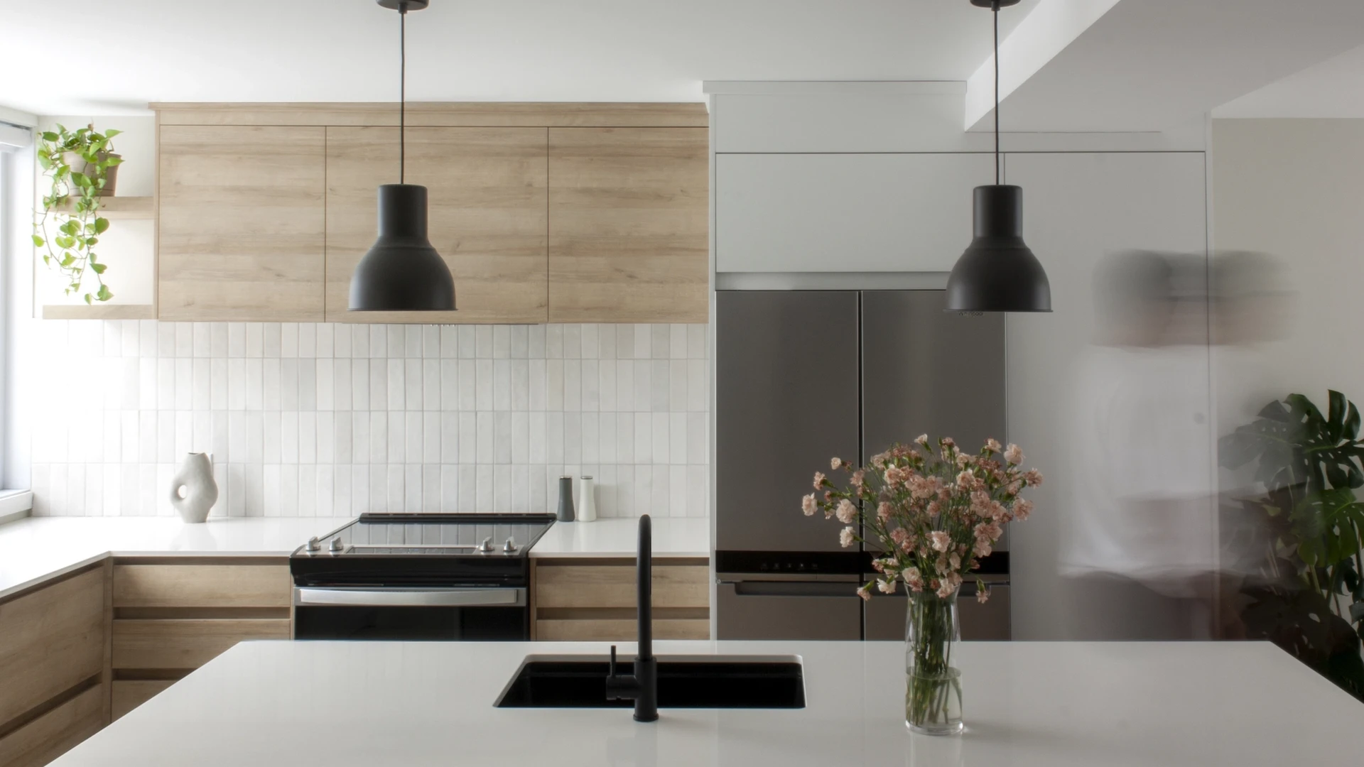 Cuisine moderne avec armoires en bois clair, luminaires noirs et plan de travail blanc, décoration minimaliste.