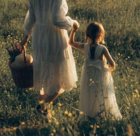 A toddler reaching up to touch her pregnant mother's belly in dappled sunlight