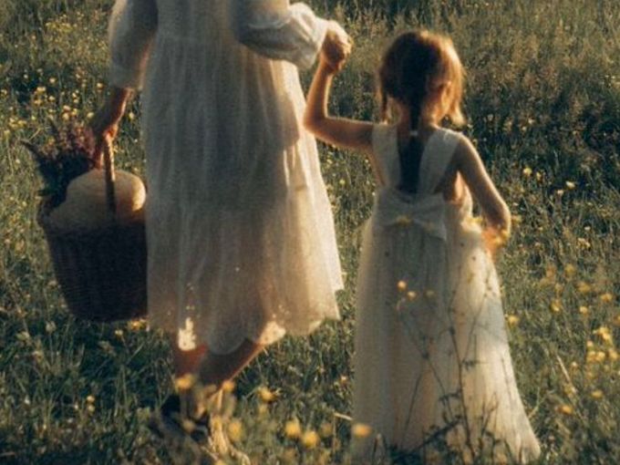 A toddler reaching up to touch her pregnant mother's belly in dappled sunlight