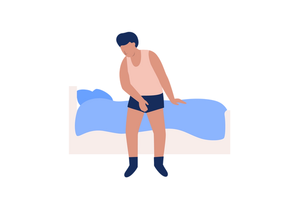 An illustration of a person sitting on the edge of a bed holding their crotch. They are wearing dark blue socks and underwear and a light pink undershirt. The bed is pink with blue sheets and blankets.