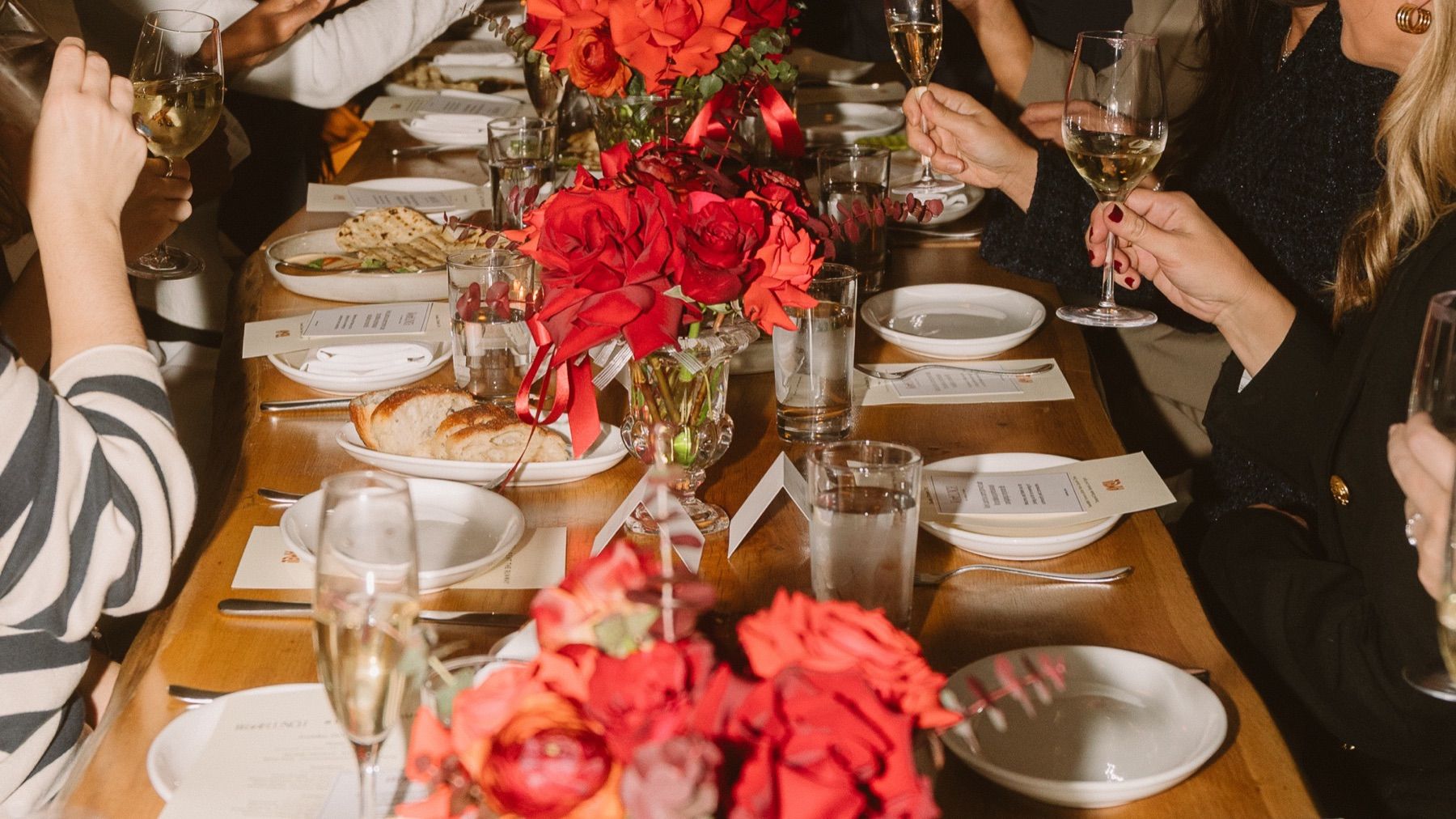 Guests raising glasses over red roses at the Rent the Runway × Work Lunch dinner