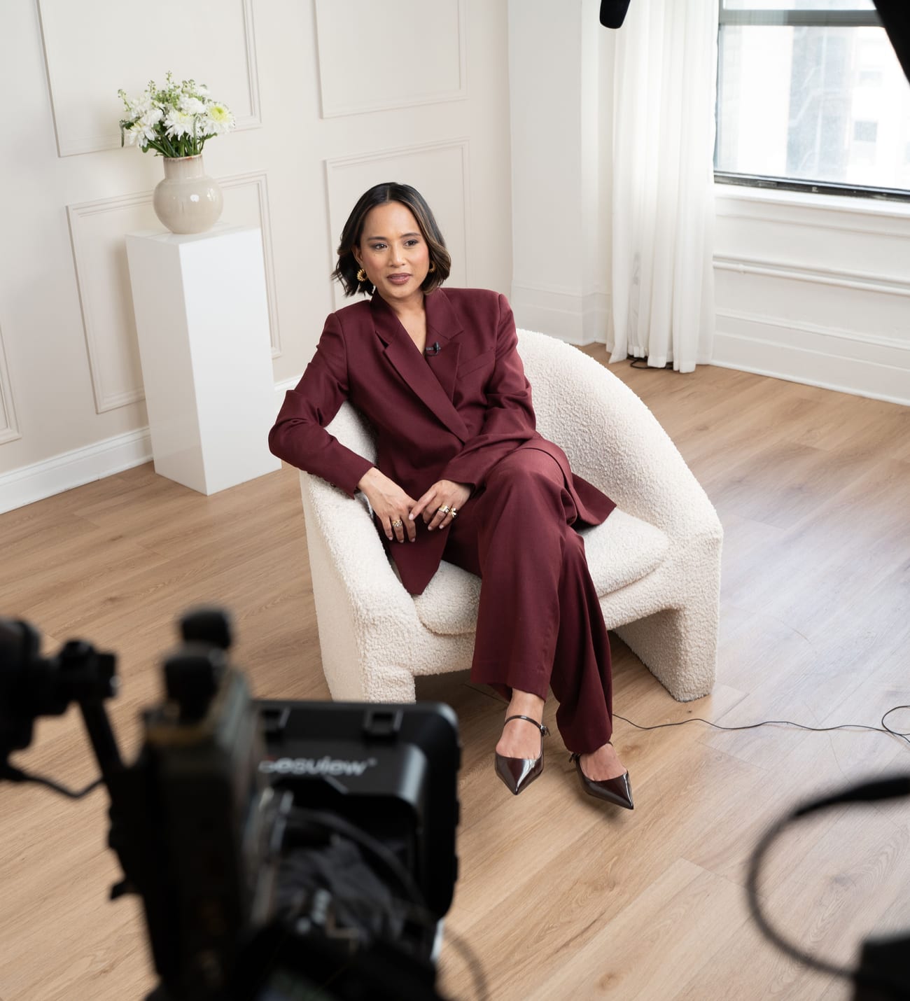 Jeanelle in a navy pinstripe shirt, seated for an interview with a camera in the foreground