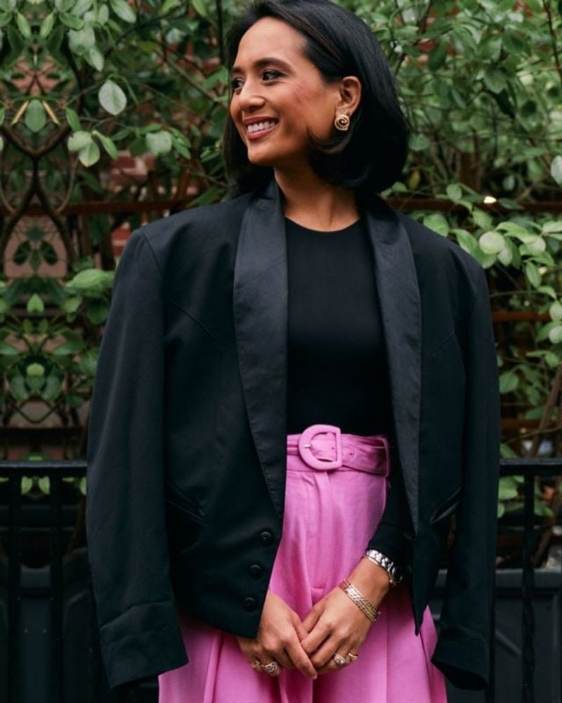 Jeanelle in a black top and pink skirt beside a New York garden