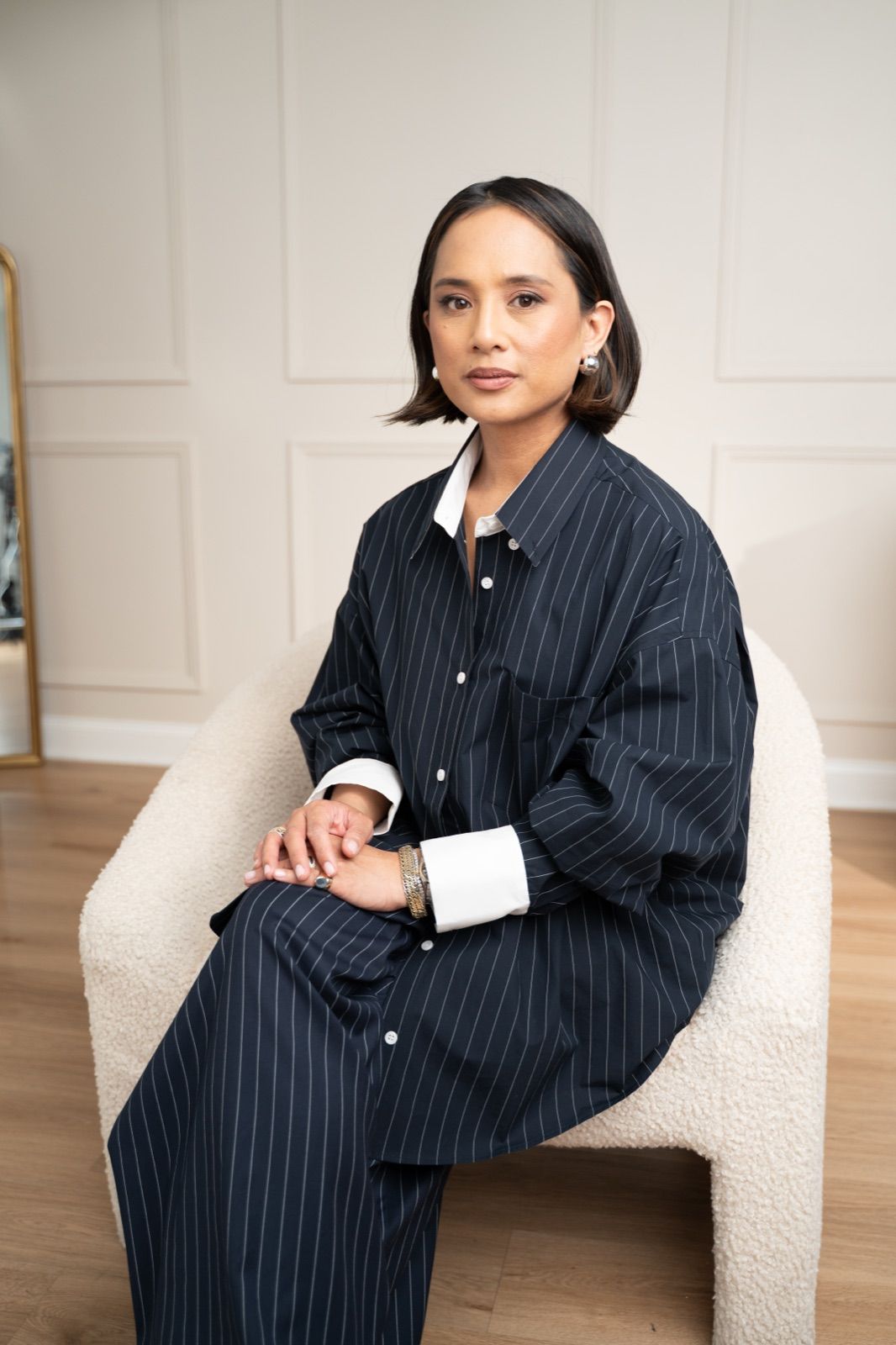 Jeanelle Teves in a navy pinstripe shirt, seated in a cream armchair