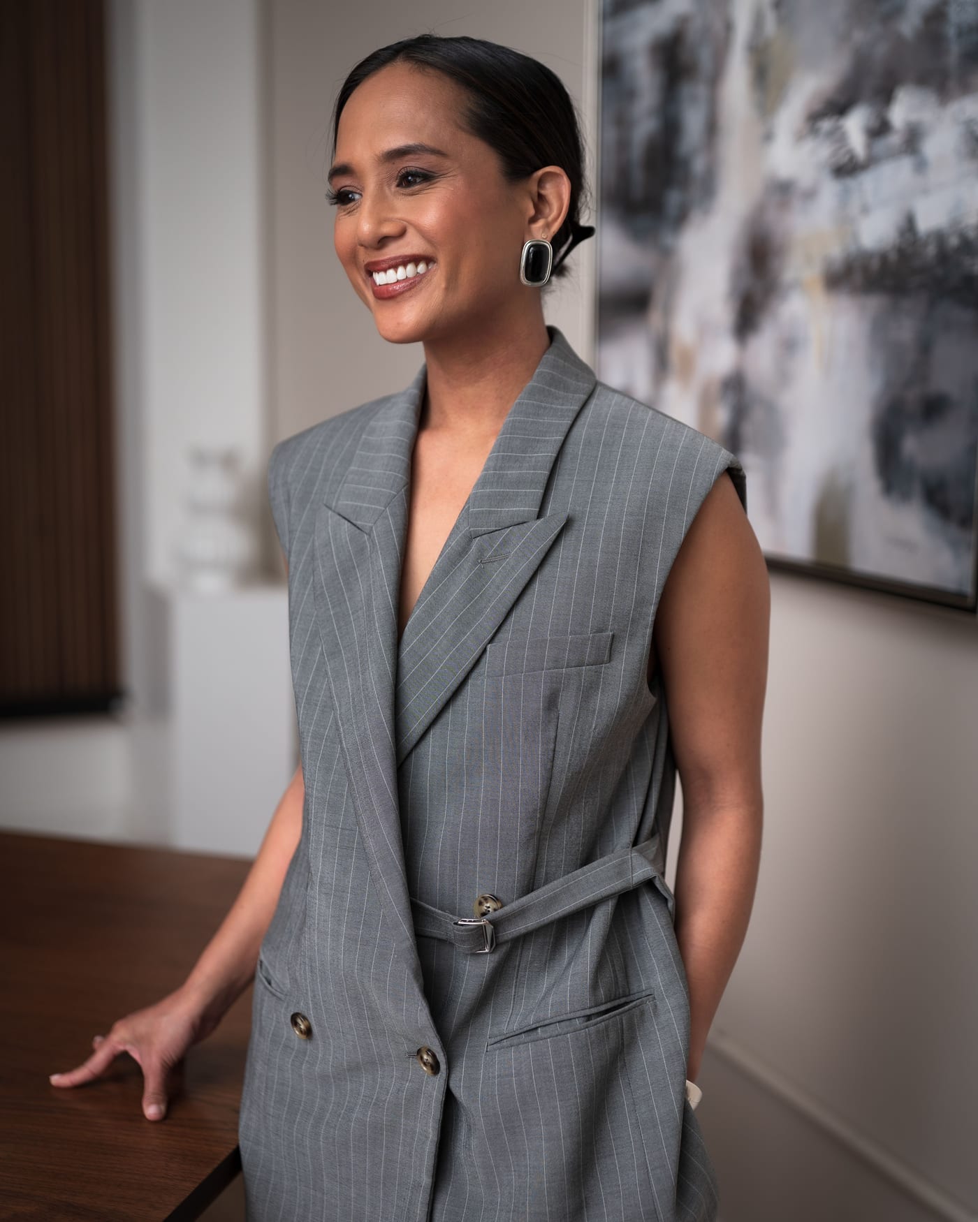 Jeanelle in a grey pinstripe vest, smiling beside a conference table