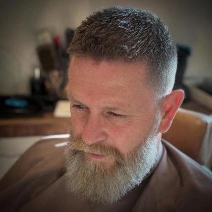 A short grey fade with a full, trimmed beard