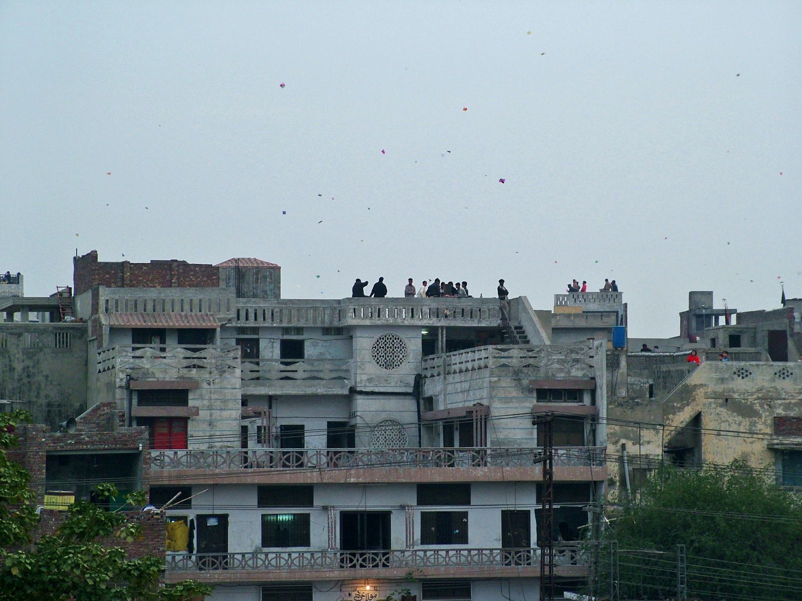 Crowded Lahore rooftops during Basant, with people flying kites and dozens of kites in the sky