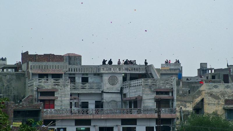 Crowded Lahore rooftops during Basant, with people flying kites and dozens of kites in the sky