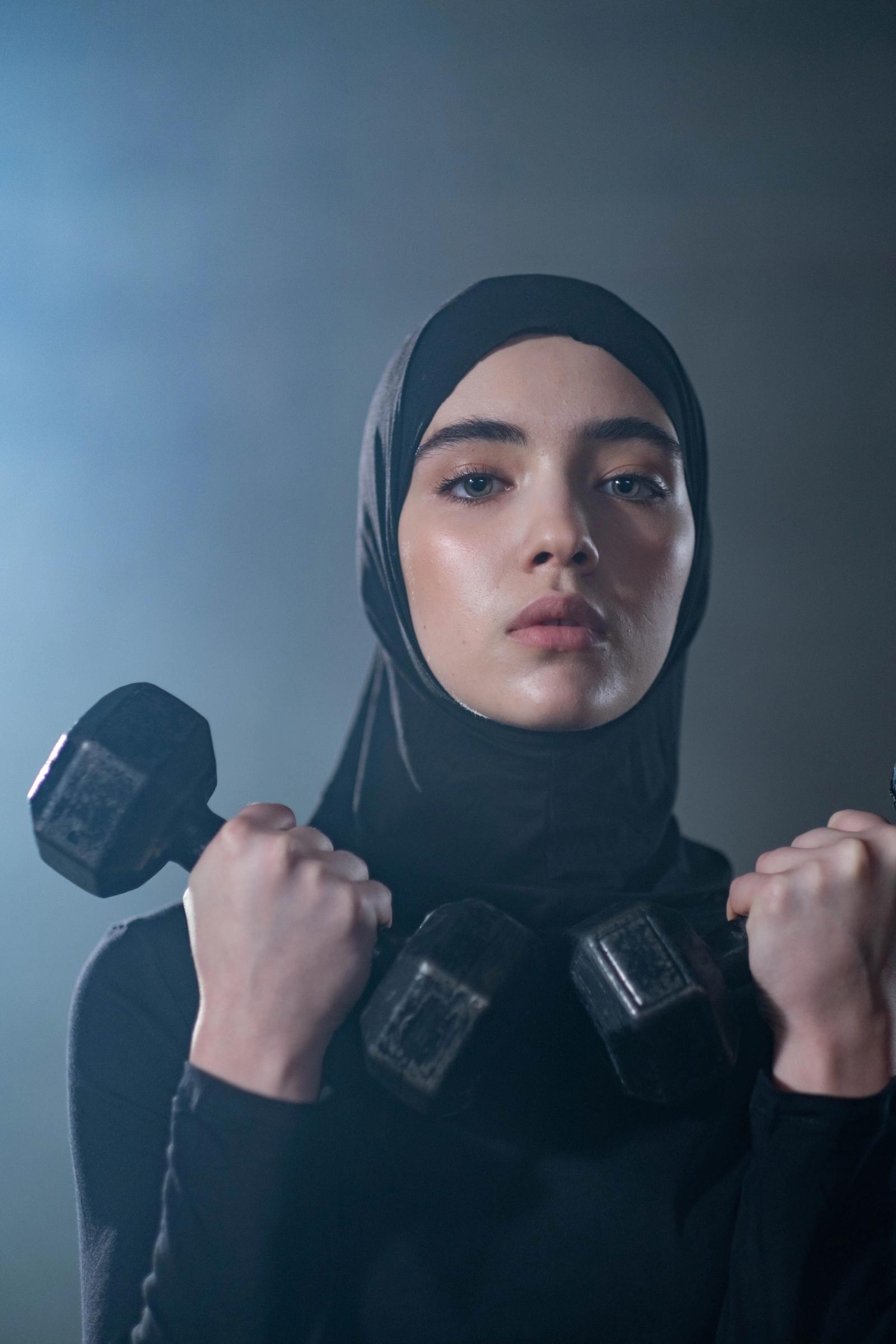 Woman in a black hijab lifting a dumbbell during a strength training workout