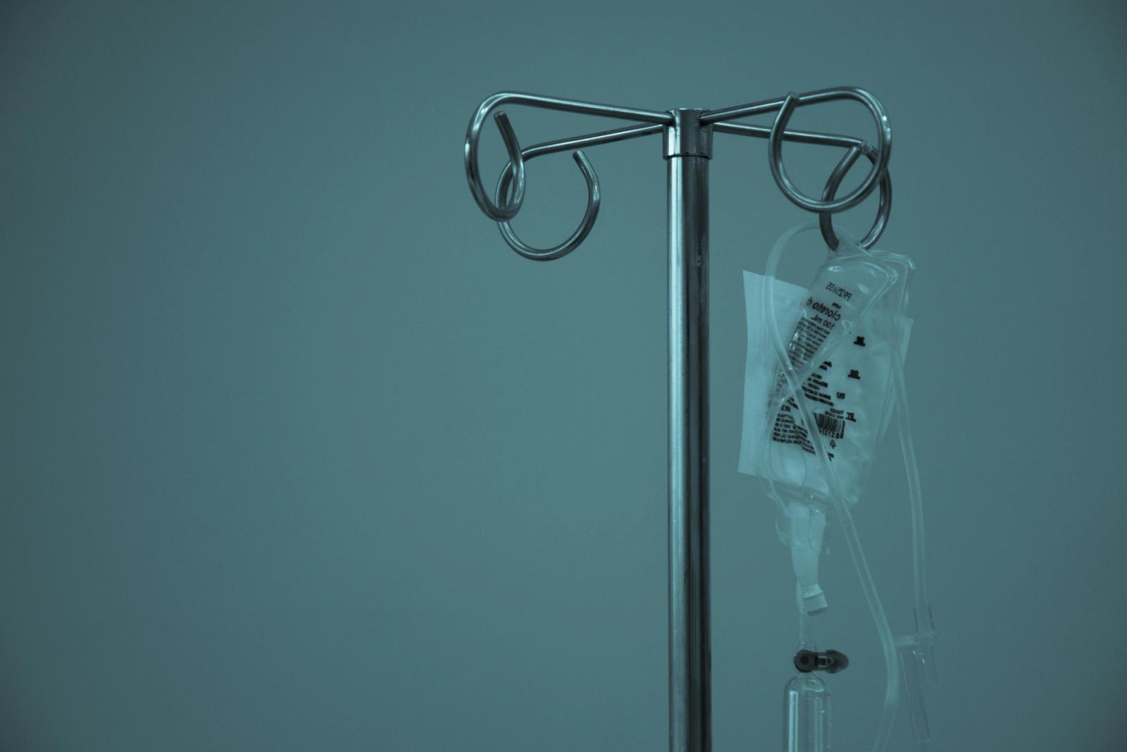 Stainless steel IV stand with a small infusion bag in a clinic, teal tones