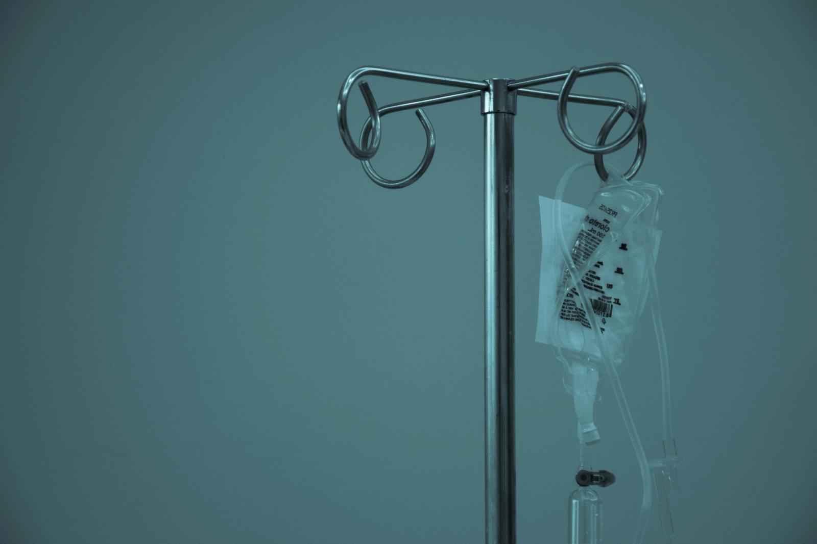 Stainless steel IV stand with a small infusion bag in a clinic, teal tones