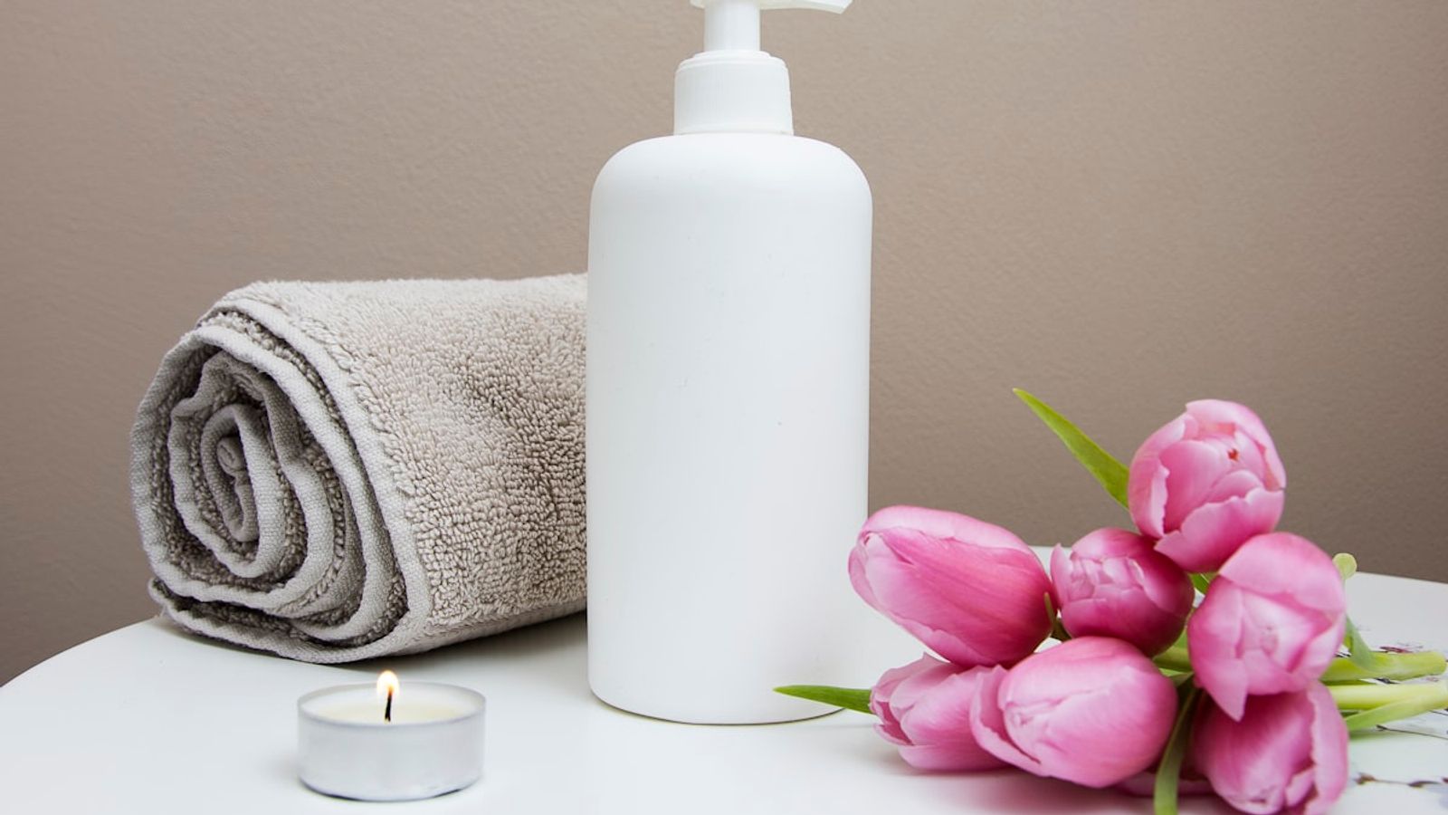 Spa treatment essentials with white rolled towels, essential massage oils, and natural exfoliating scrub in a bowl