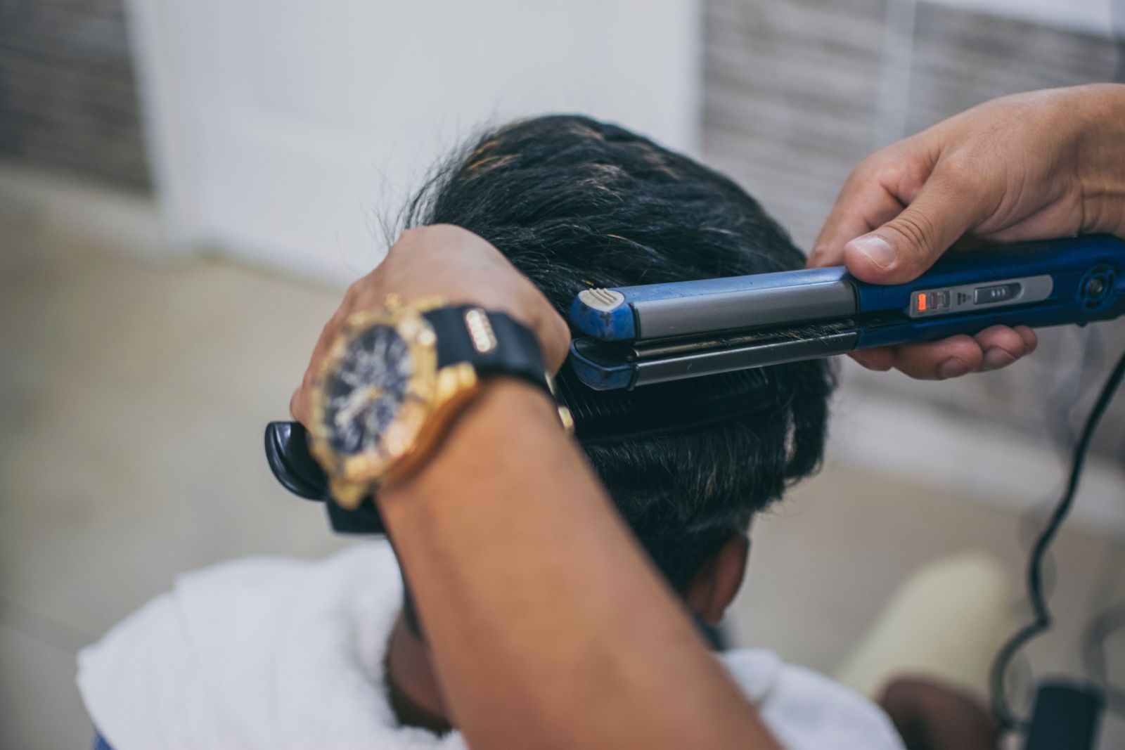 Stylist running a flat iron through the thick black hair on the back of a man's head in a salon