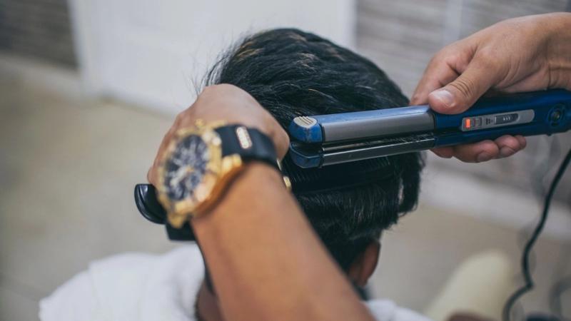 Stylist running a flat iron through the thick black hair on the back of a man's head in a salon