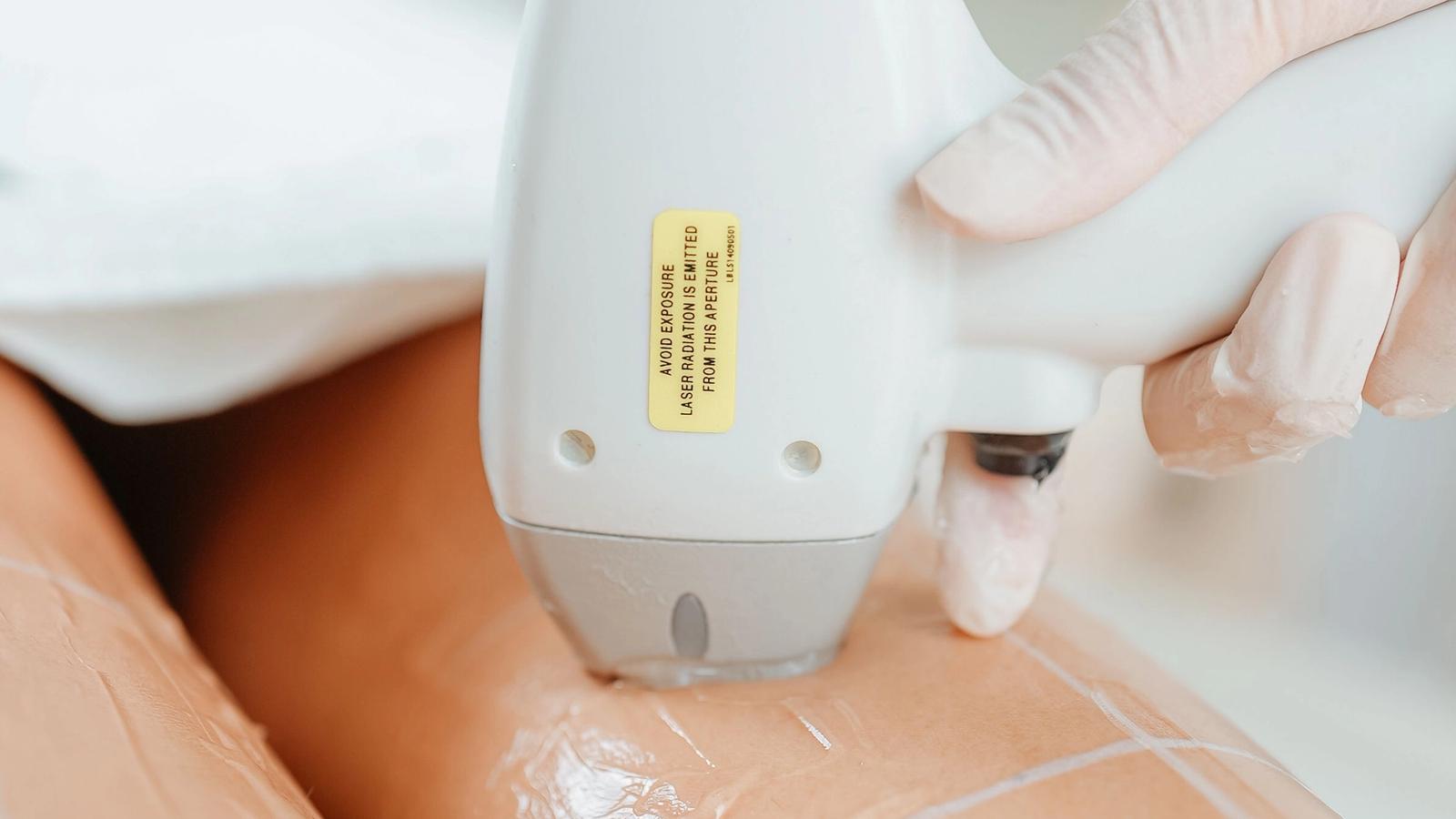 Close-up of a laser hair removal handpiece being applied to a client's leg in a clinic