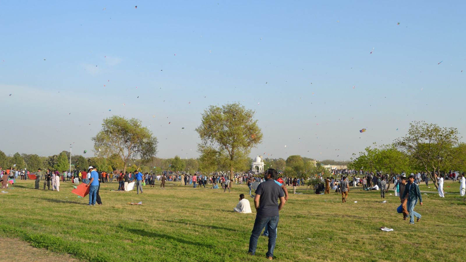 People flying kites on a wide park lawn during Basant at F-9 Park, Islamabad, with dozens of kites in a clear sky