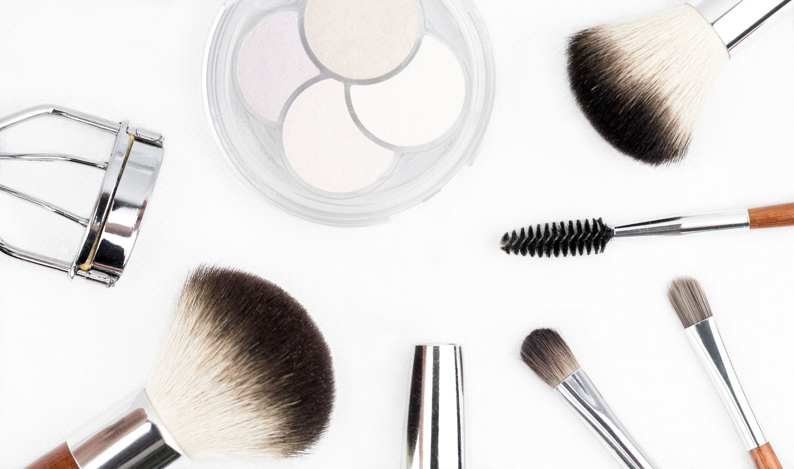 Flat lay of makeup brushes, an eyelash curler and an eyeshadow palette on a white surface
