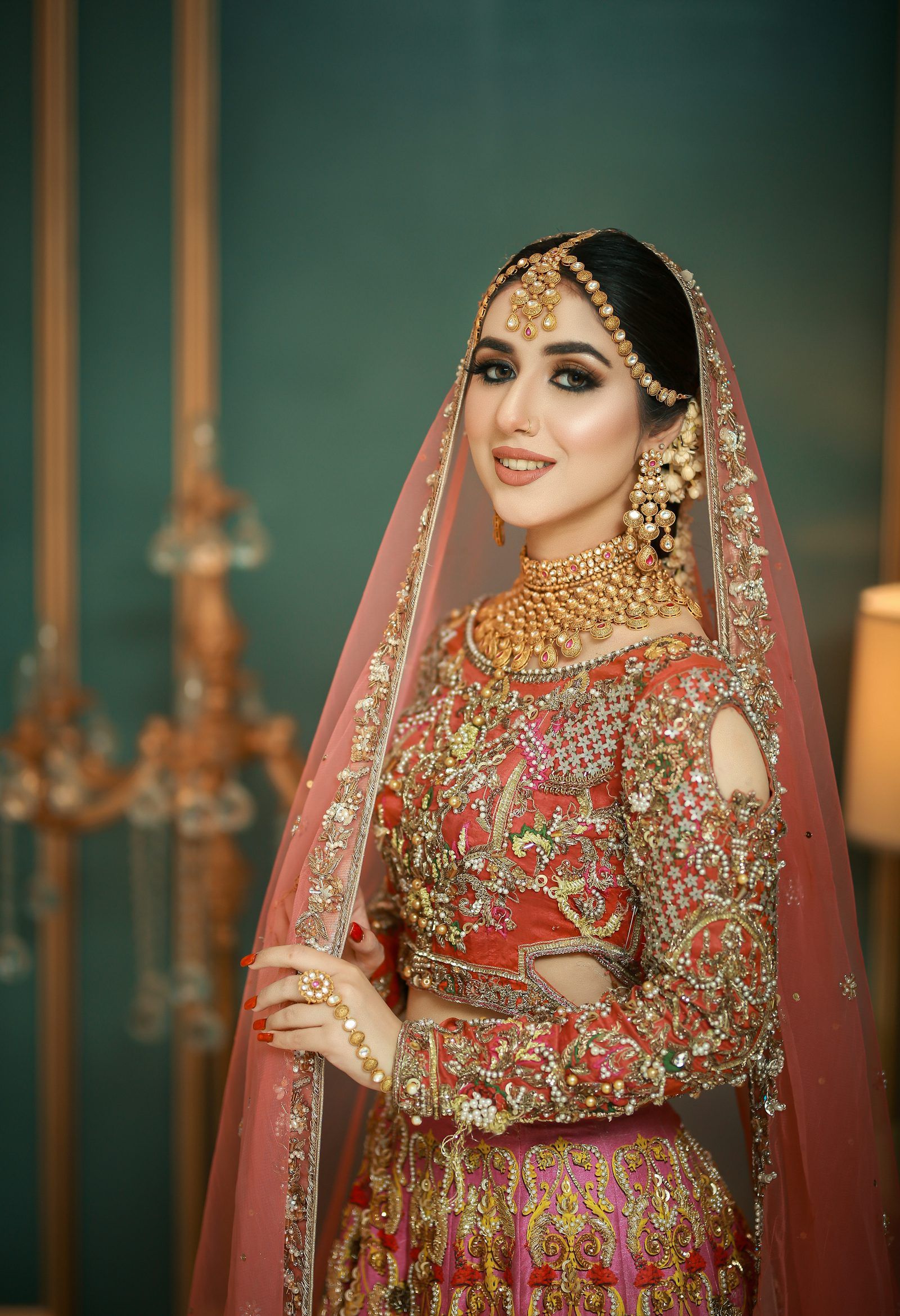 A bride in an embroidered red and gold outfit with gold jewellery, photographed in a Lahore studio