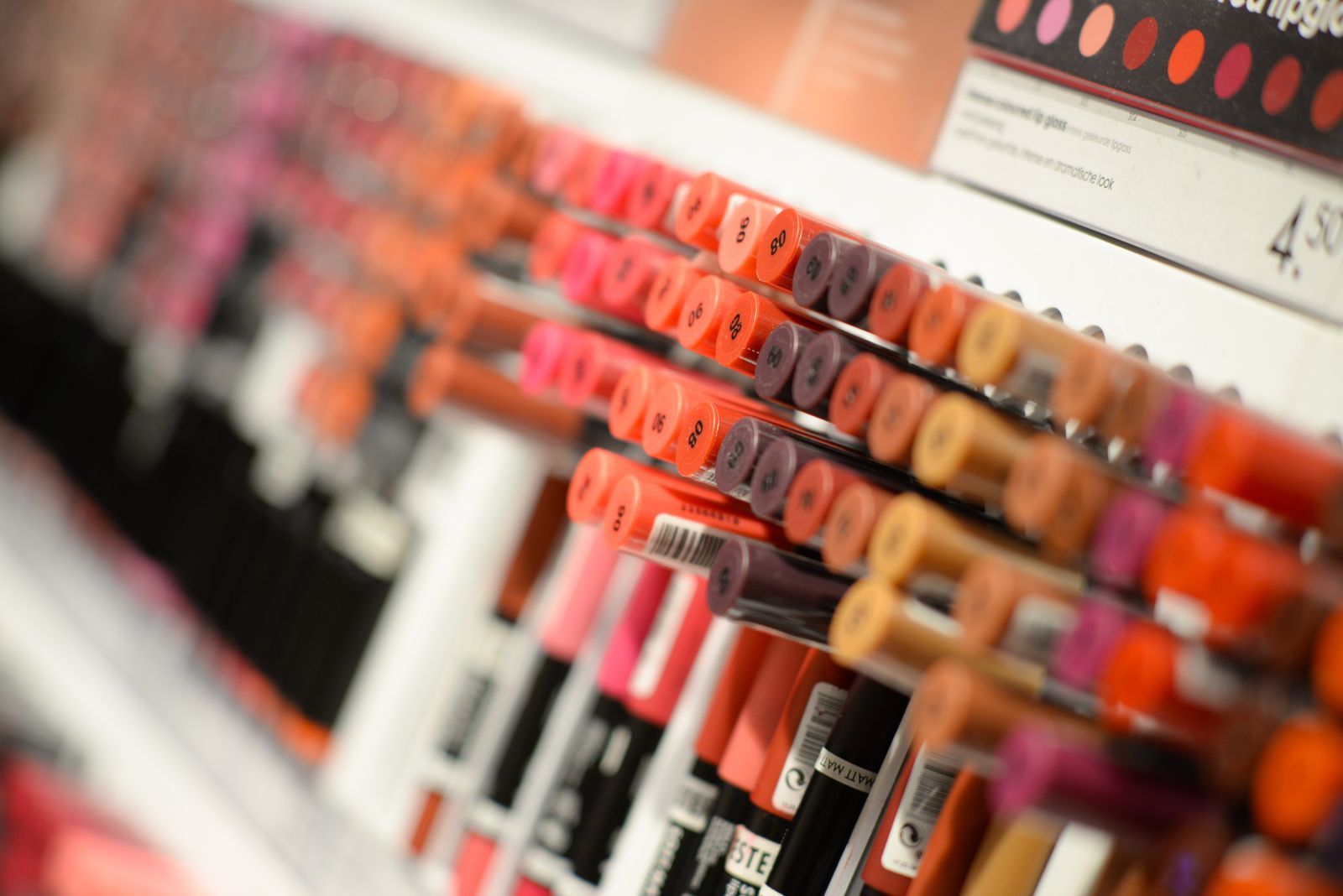 Rows of lipsticks and lip glosses on a retail cosmetics display shelf