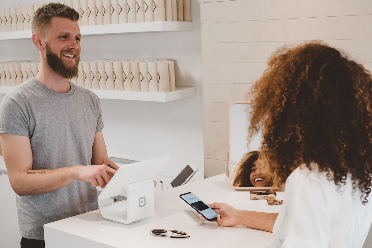 A shop owner at the counter while a customer pays by phone