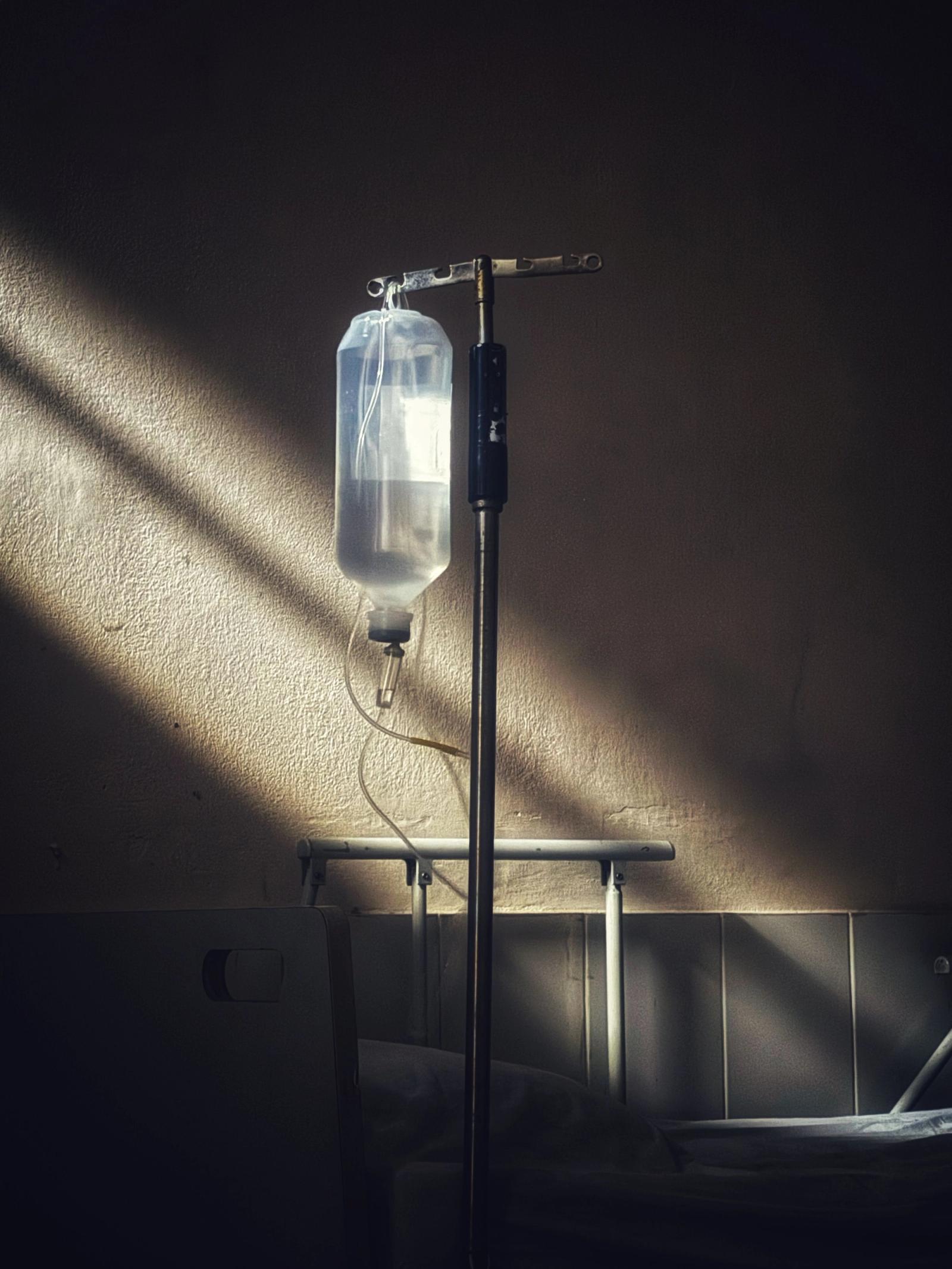 Intravenous drip bottle hanging on a stand in a dimly lit clinic room