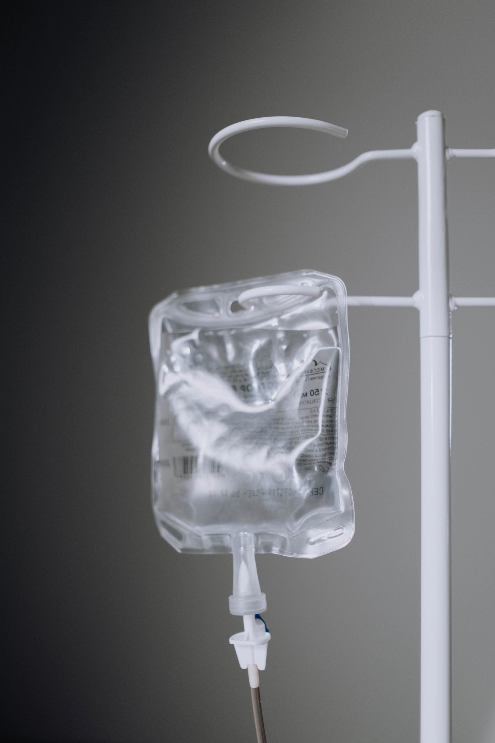 Close-up of a saline bag hanging on a white IV pole against a grey wall
