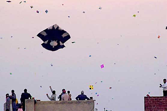 Kite fliers on a Lahore rooftop with dozens of kites in the sky during Basant