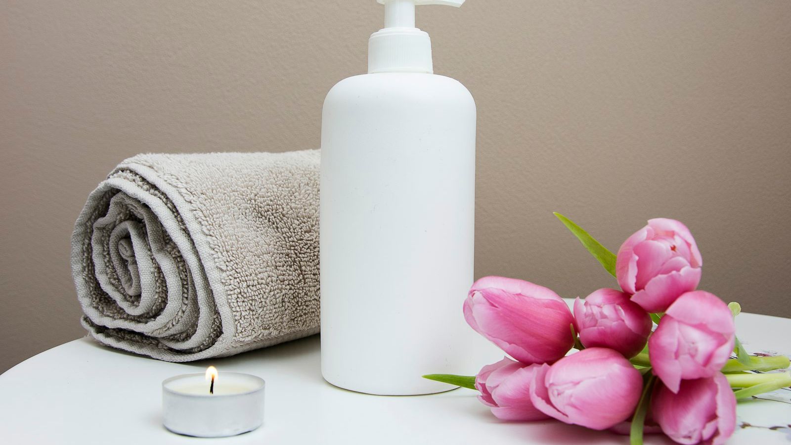 Spa towel, lotion bottle and pink flowers arranged for a massage session