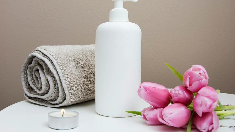 Spa towel, lotion bottle and pink flowers arranged for a massage session