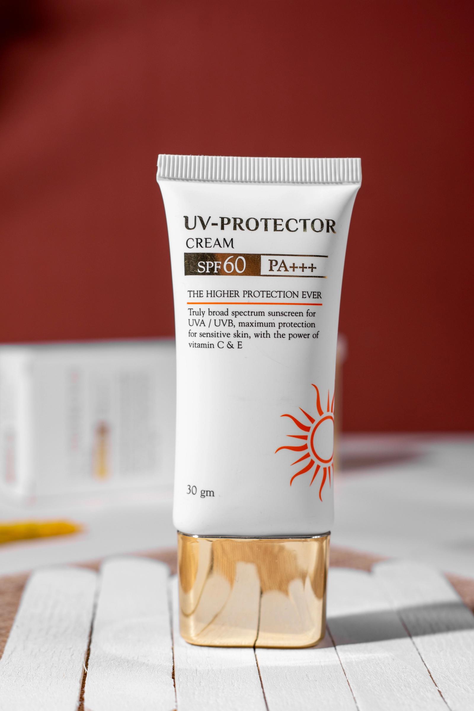 A white SPF 60 broad spectrum sunscreen tube standing upright on white wooden slats against a deep red background